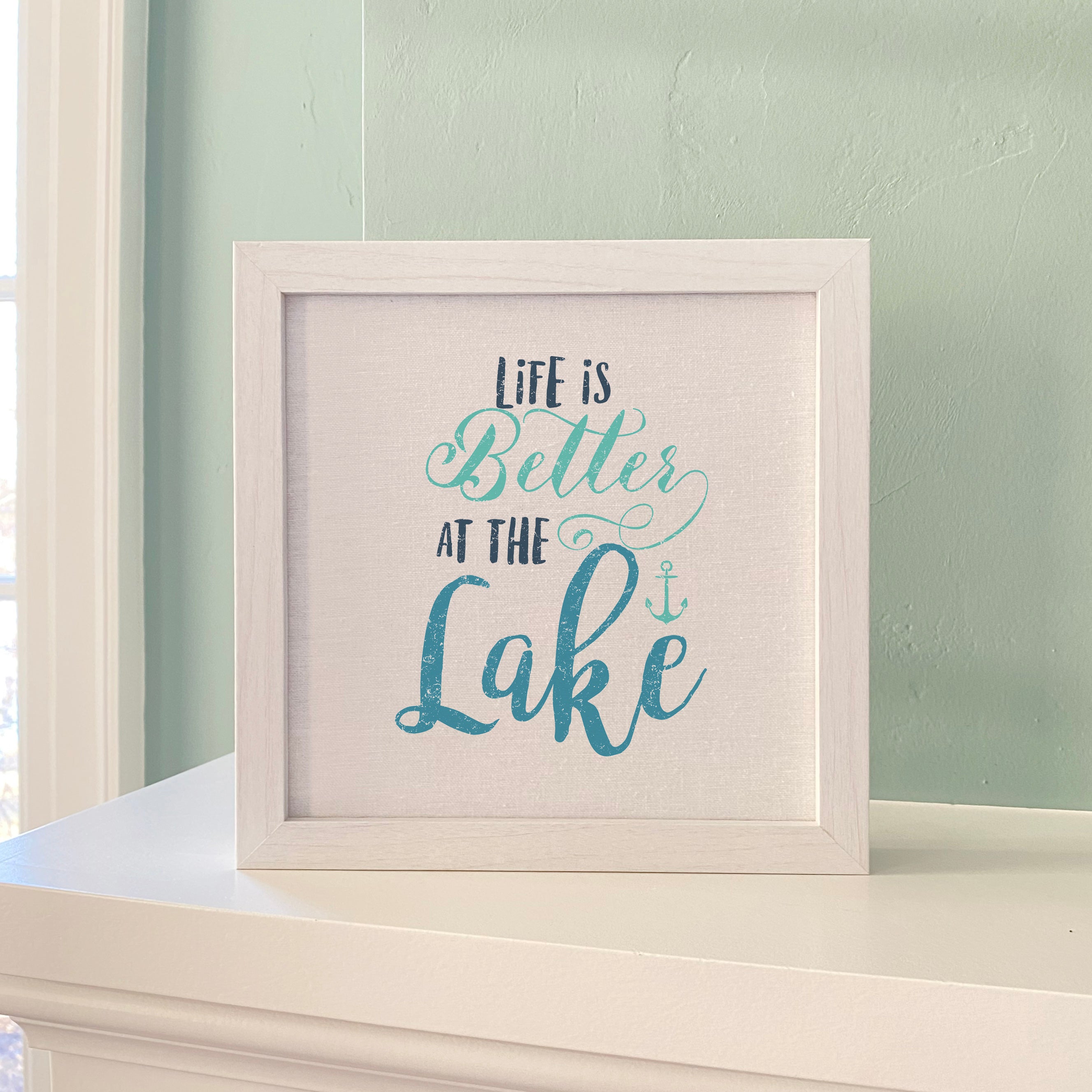 Framed sign reading 'Life is Better at the Lake' with a stylized wood frame, displayed on a shelf.