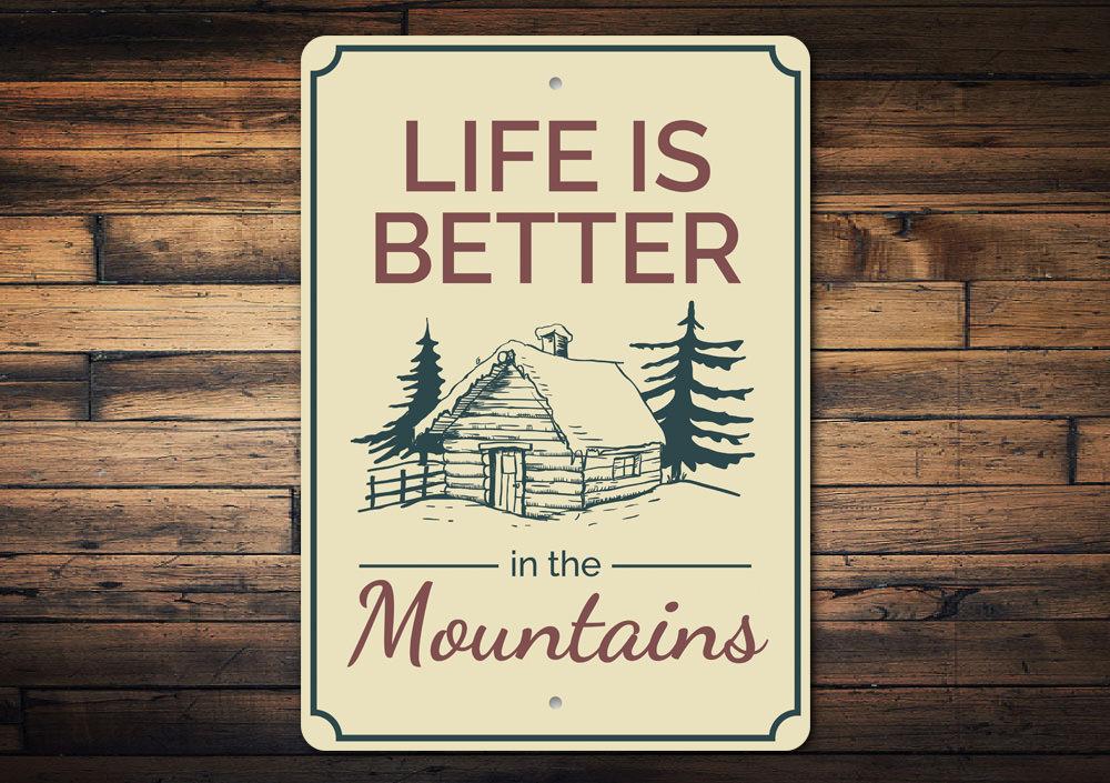 A decorative metal sign that reads 'Life is Better in the Mountains', showcasing a scenic mountain backdrop, perfect for cabin decor.