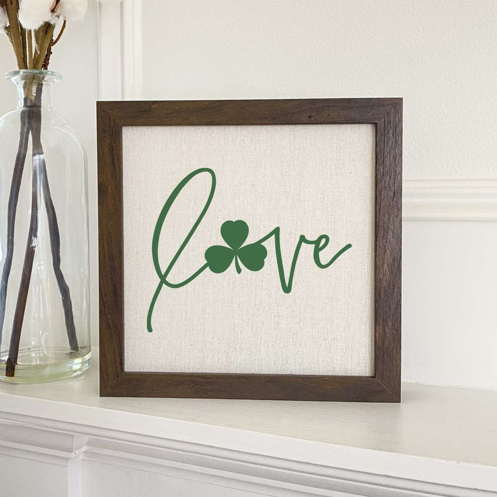 Framed sign featuring a shamrock accent and the word 'Love', set in a stylish wood frame with a linen-look background.