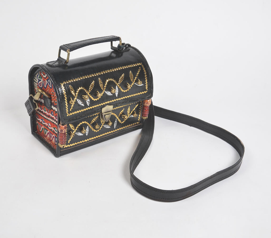 Handcrafted black leather bag with metallic bells and intricate punchwork, showcasing Kutch artisan craftsmanship.