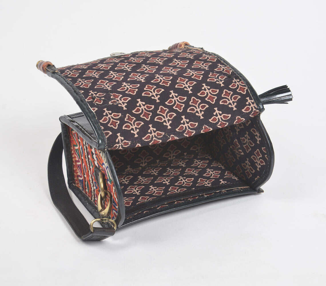 Handcrafted black leather bag with metallic bells and intricate punchwork, showcasing Kutch artisan craftsmanship.
