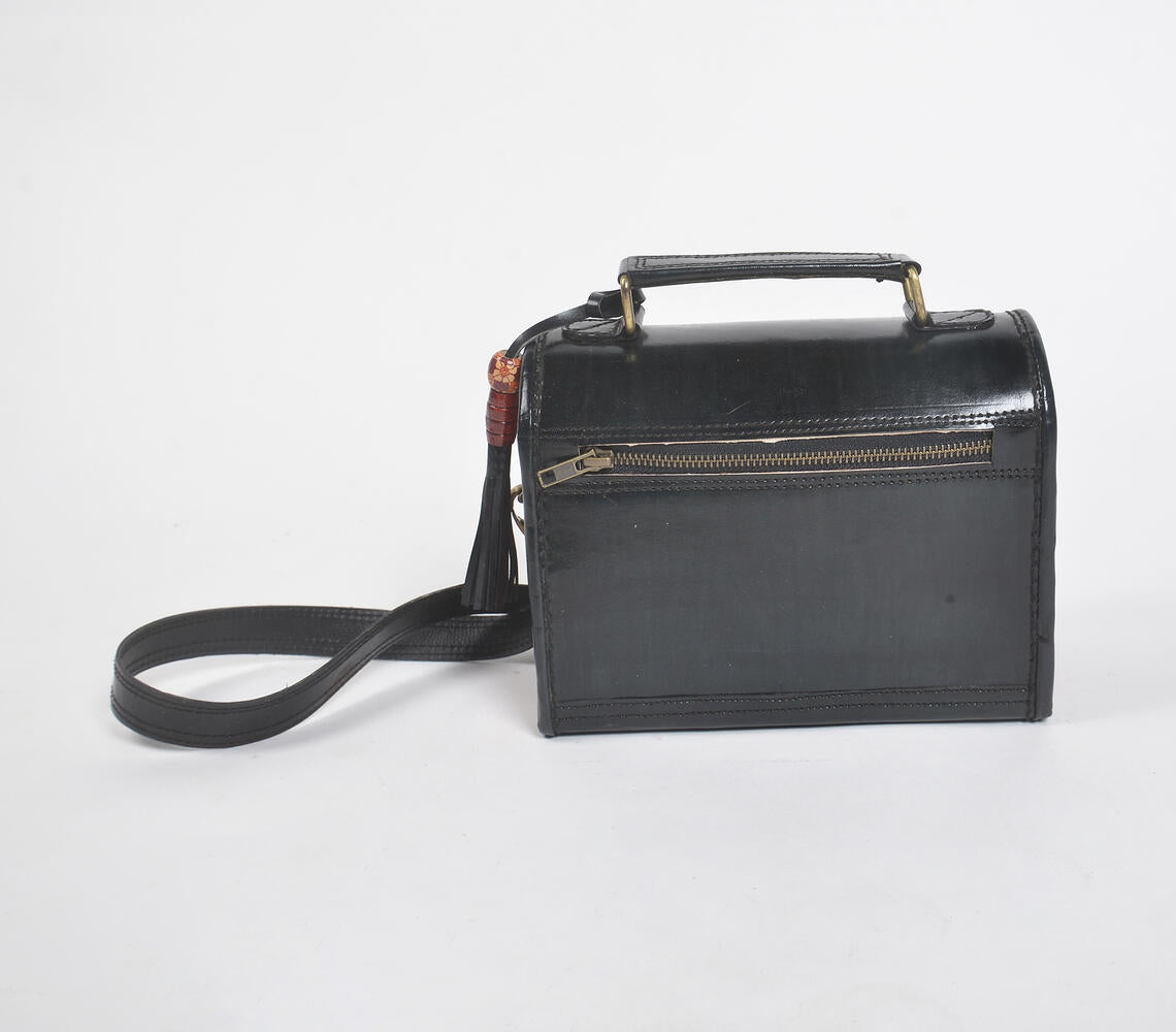 Handcrafted black leather bag with metallic bells and intricate punchwork, showcasing Kutch artisan craftsmanship.