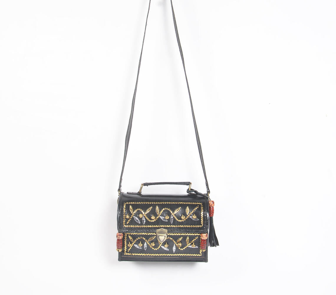 Handcrafted black leather bag with metallic bells and intricate punchwork, showcasing Kutch artisan craftsmanship.