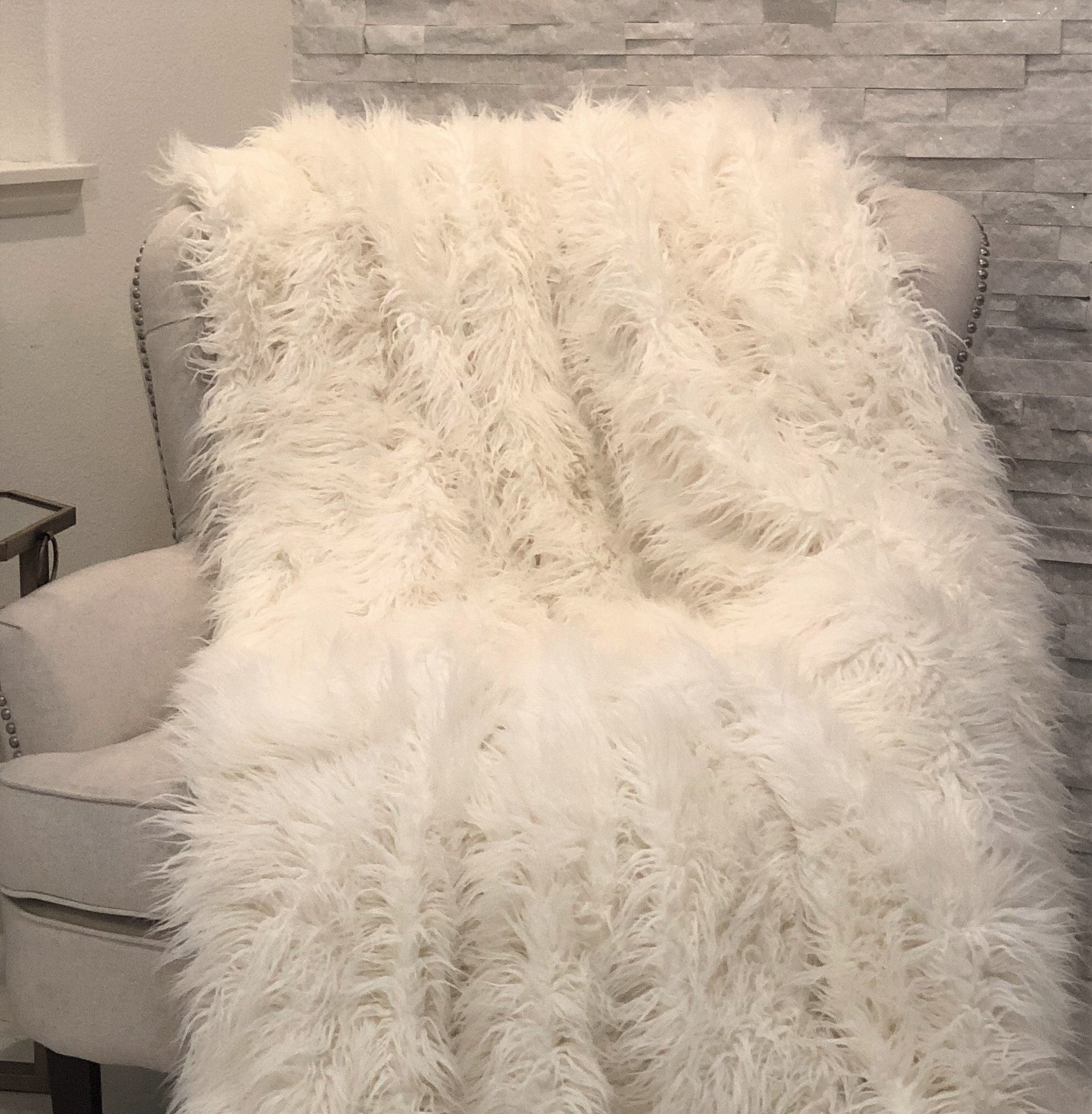 A luxurious white Mongolian faux fur throw blanket with long, curly fibers and soft microfiber backing, perfect for cozying up any room.