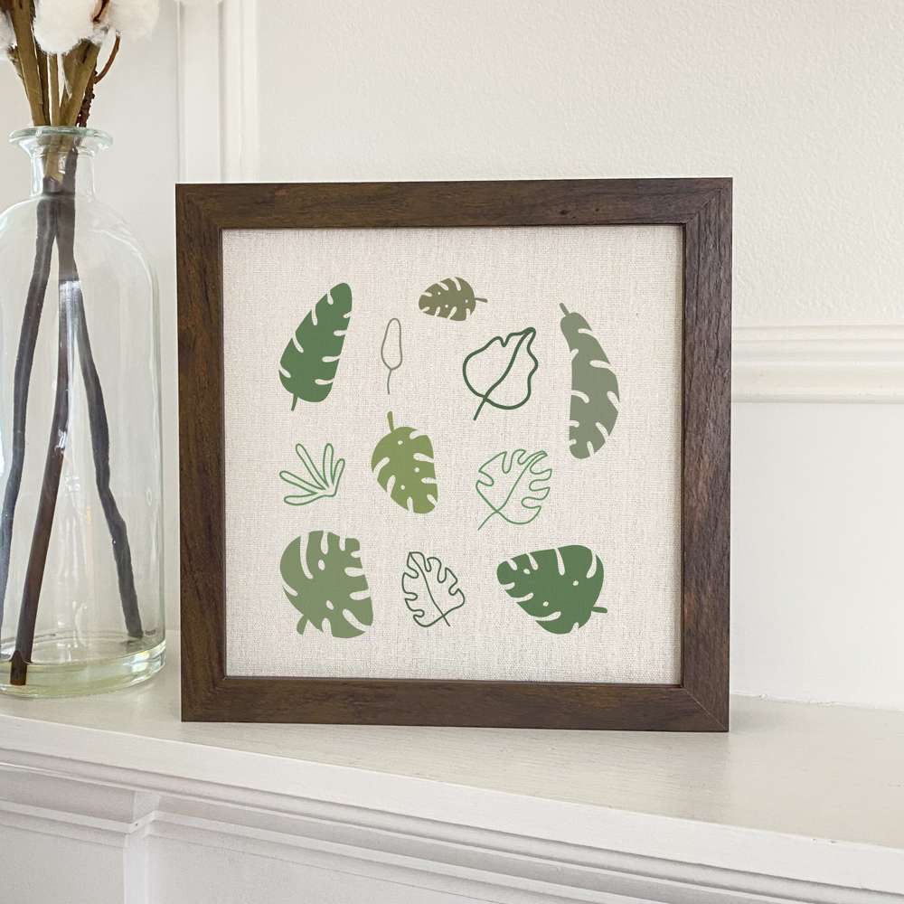Framed sign featuring Monstera palm leaves with a natural wood frame, perfect for home decor.