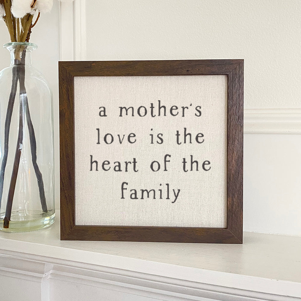 Framed sign reading 'Mother's Love is the heart' with a natural linen background and wooden frame options.