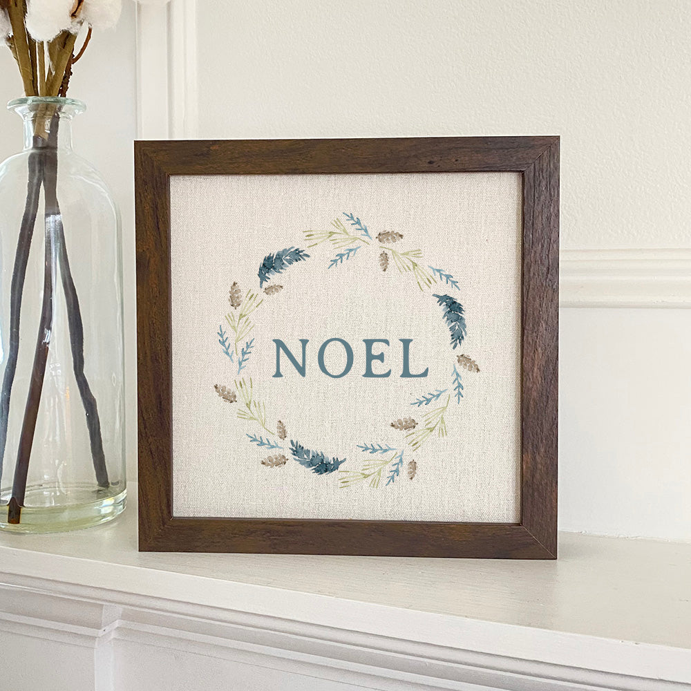 Noel Pine Wreath framed sign with a stylized wood frame, featuring a linen-look background and eco-friendly ink printing.