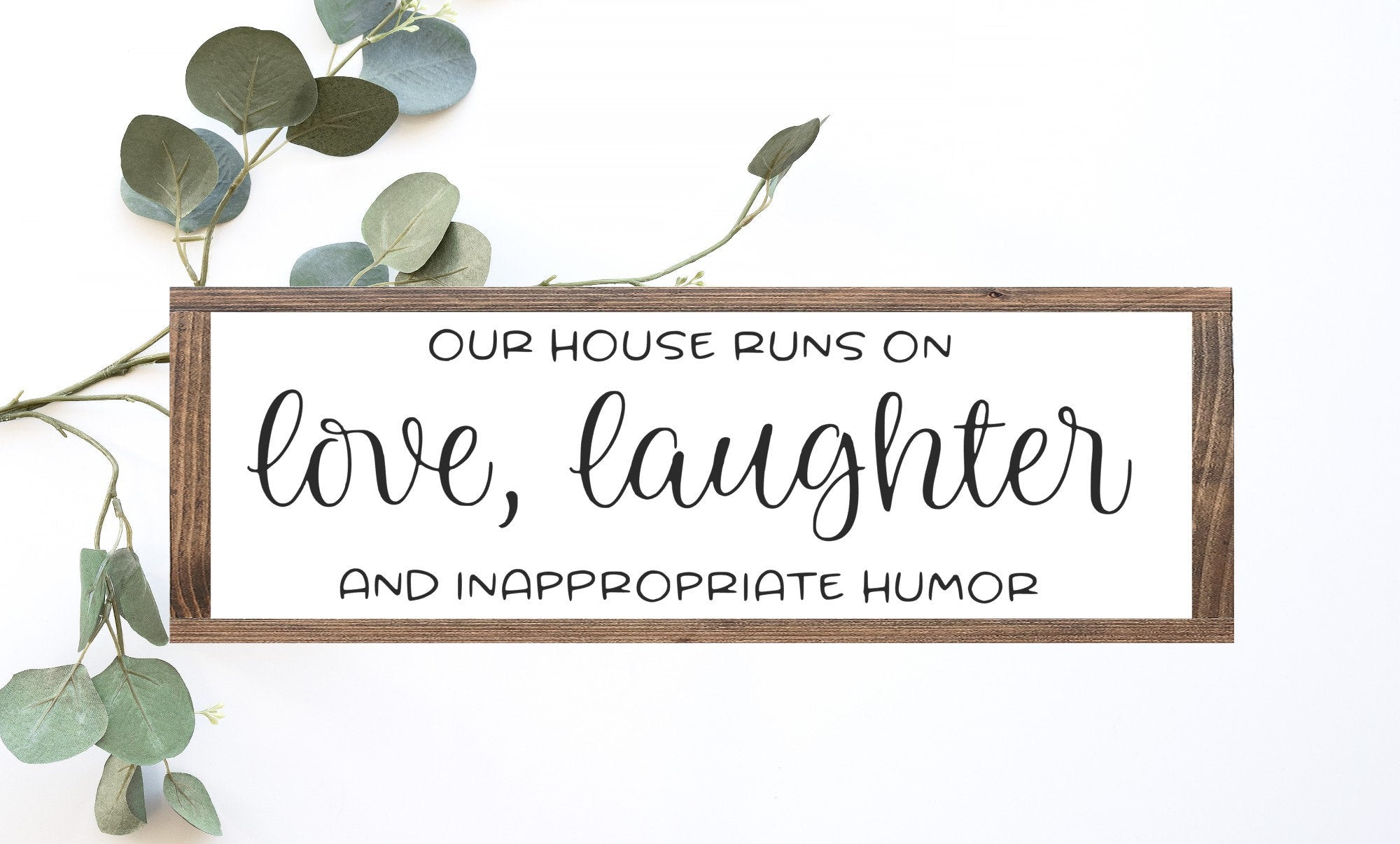 Handmade wood sign reading 'Our House Runs On Love, Laughter, and Inappropriate Humor' with a matte white background and rustic wood frame.