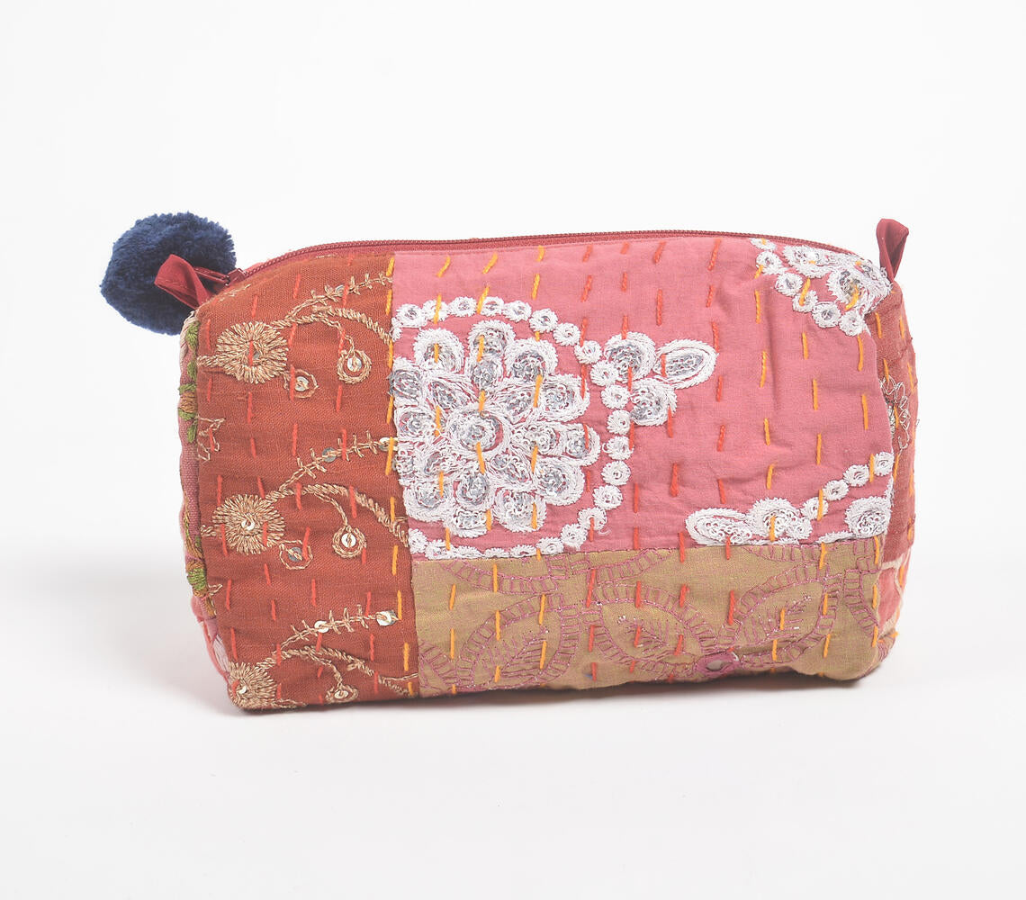 A vibrant red eco-friendly cosmetic pouch made from patchwork cotton, featuring a pompom zipper pull and unique fabric patterns.