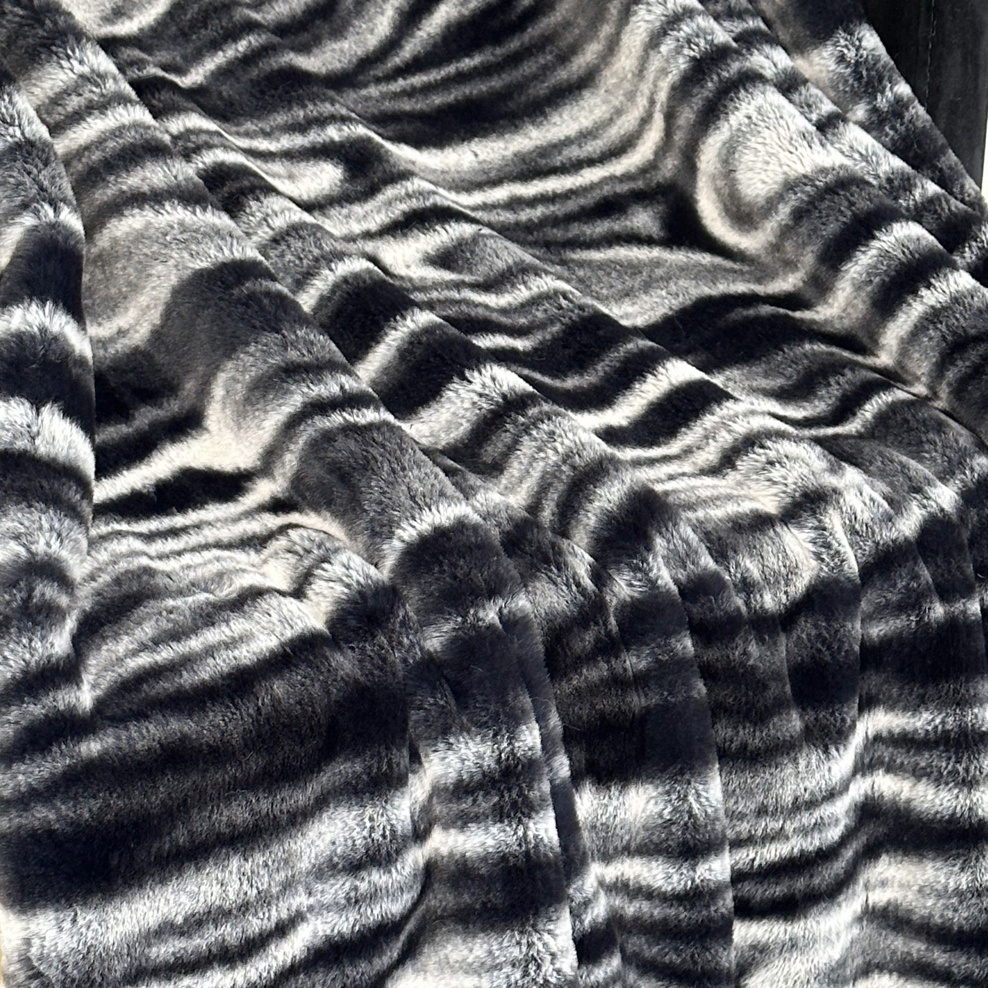 Plutus Black White Galaxy Faux Fur Luxury Throw Blanket draped elegantly over a sofa, showcasing its plush texture and stylish design.