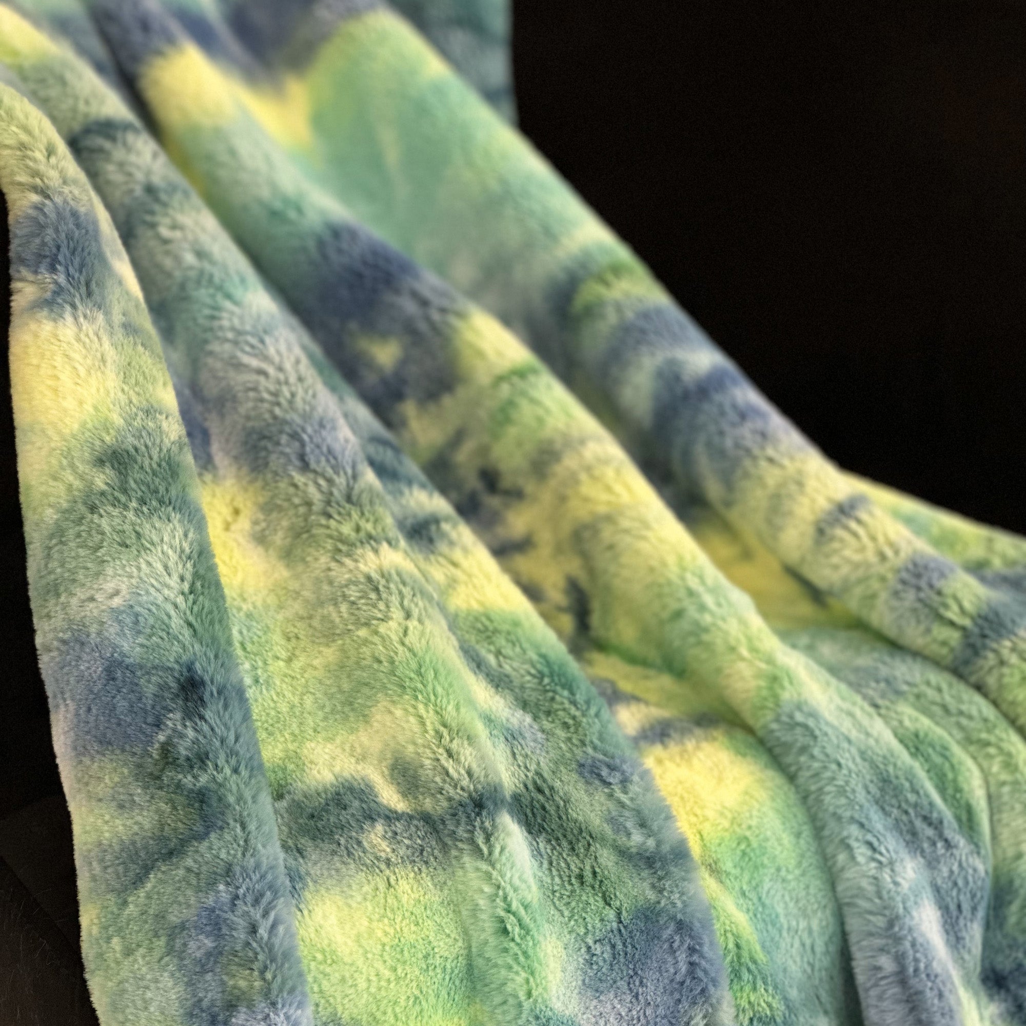 Plutus Green Yellow Blue Northern Lights Faux Fur Luxury Throw Blanket draped elegantly over a couch, showcasing its vibrant colors and plush texture.