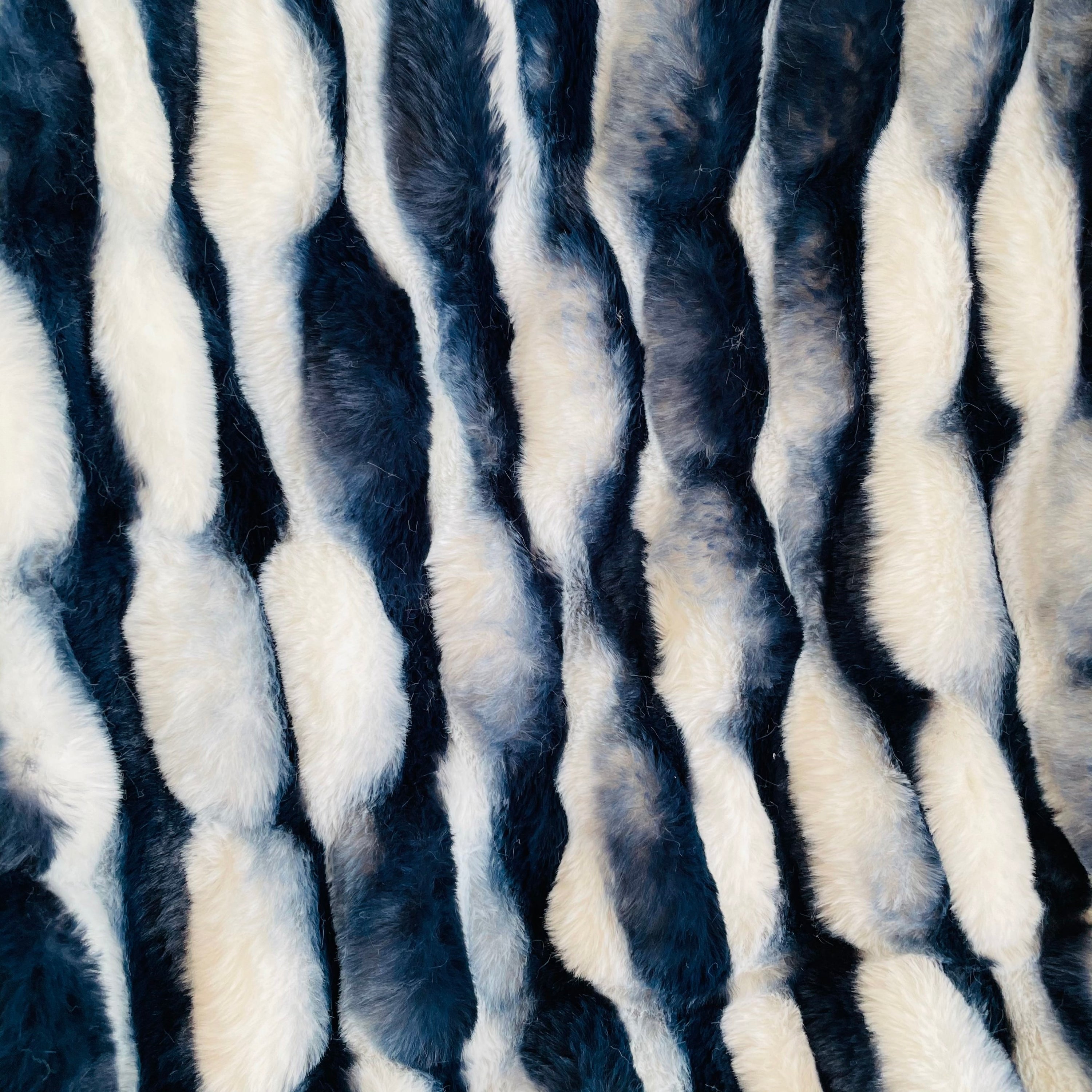 Plutus White Navy Snow Chinchilla Faux Fur Luxury Throw Blanket draped elegantly on a couch, showcasing its soft texture and stylish color combination.