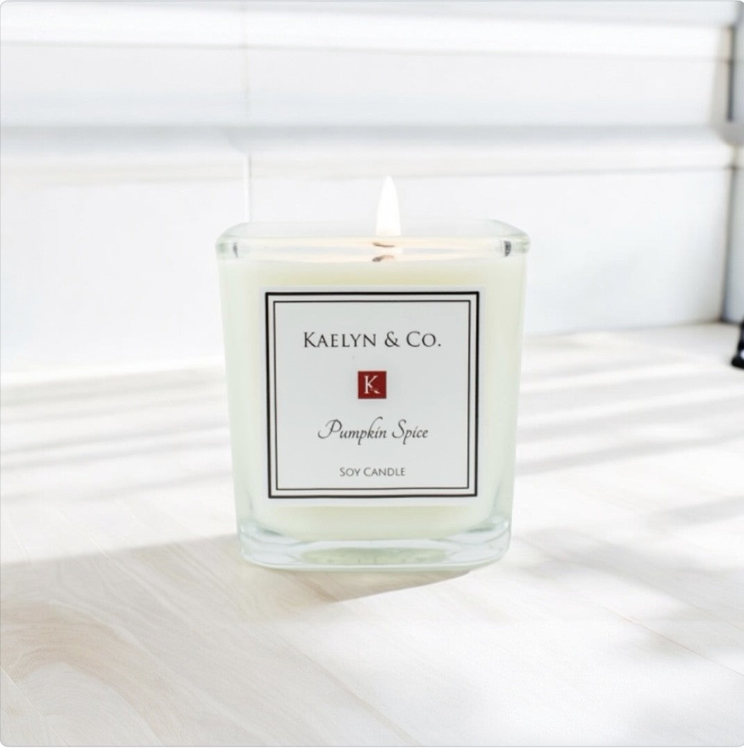 A small cube candle in pumpkin spice scent, featuring warm autumn colors and a cozy design, perfect for fall decor.