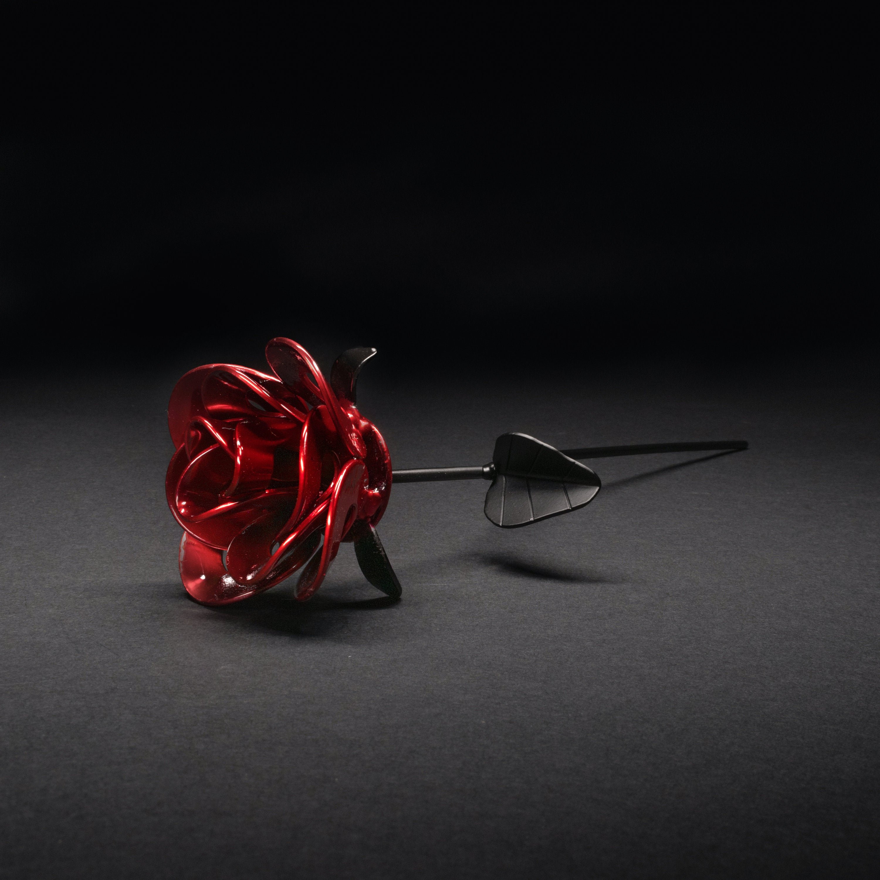 A handcrafted red and black metal rose made from recycled washers and wire, showcasing a lustrous metallic finish and a light green stem, elegantly packaged in a clear gift box.