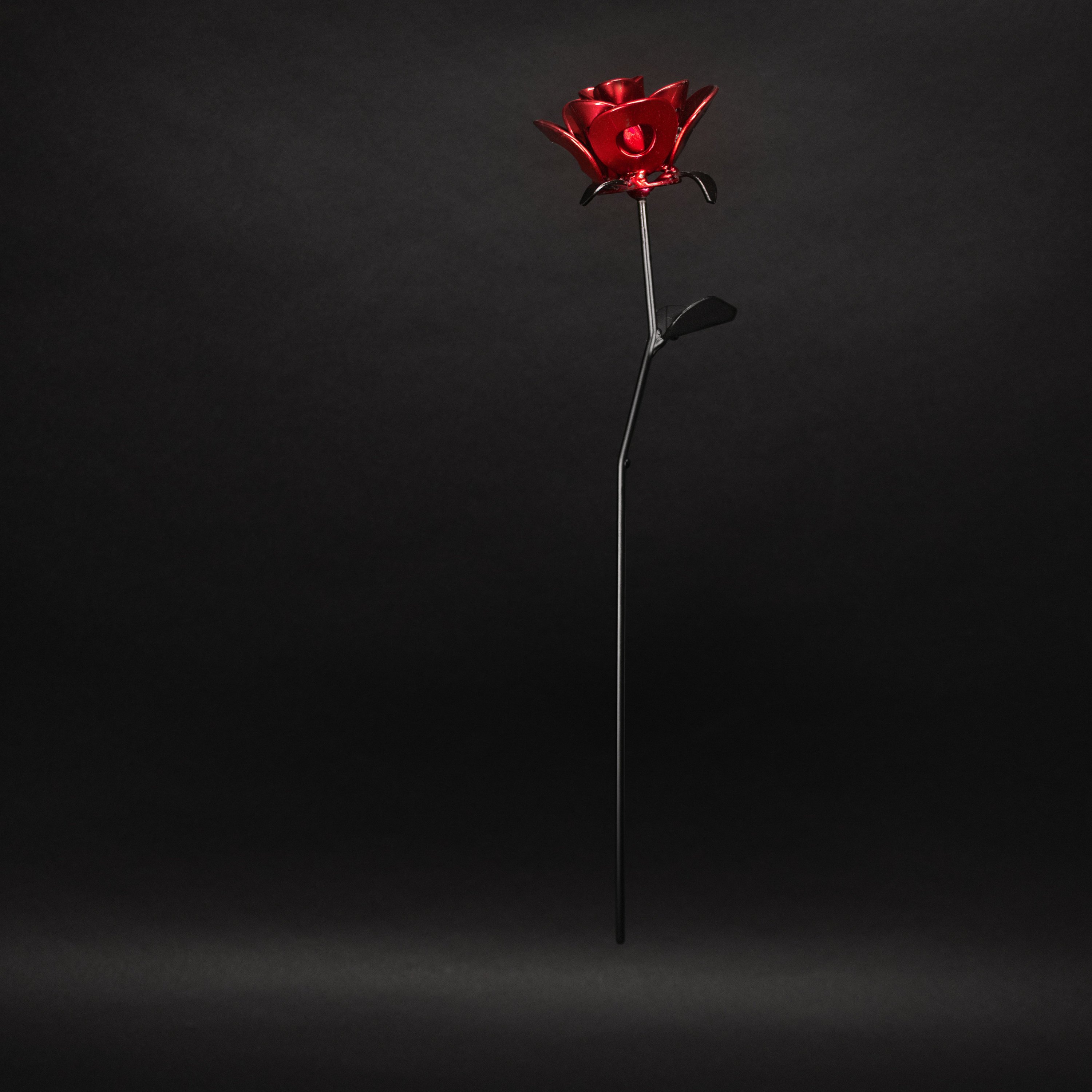 A handcrafted red and black metal rose made from recycled washers and wire, showcasing a lustrous metallic finish and a light green stem, elegantly packaged in a clear gift box.