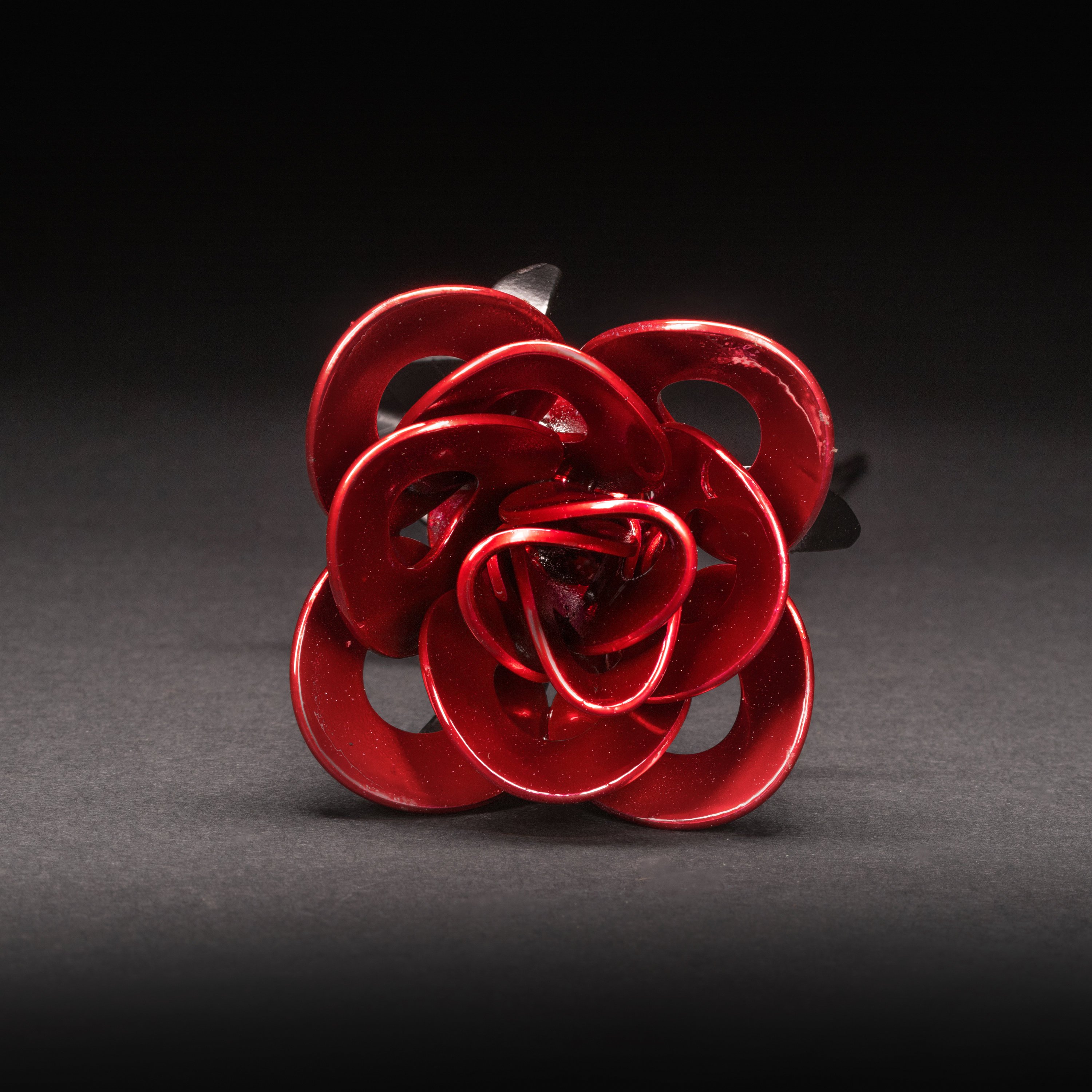 A handcrafted red and black metal rose made from recycled washers and wire, showcasing a lustrous metallic finish and a light green stem, elegantly packaged in a clear gift box.