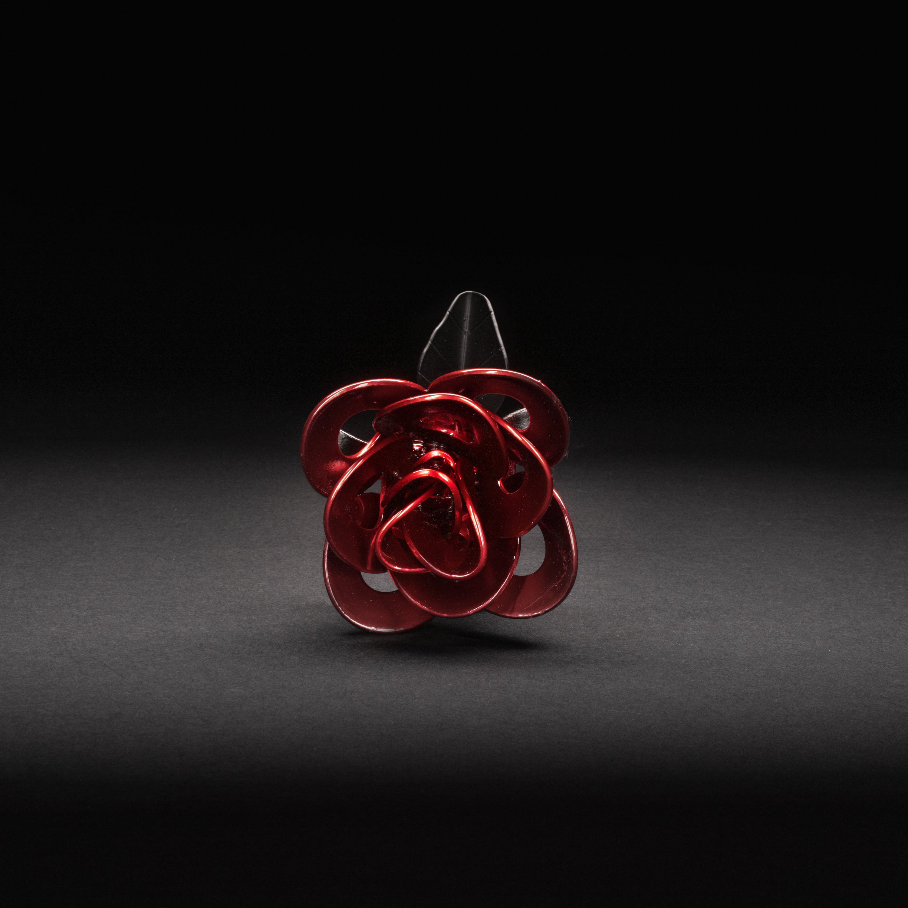 A handcrafted red and black metal rose made from recycled washers and wire, showcasing a lustrous metallic finish and a light green stem, elegantly packaged in a clear gift box.