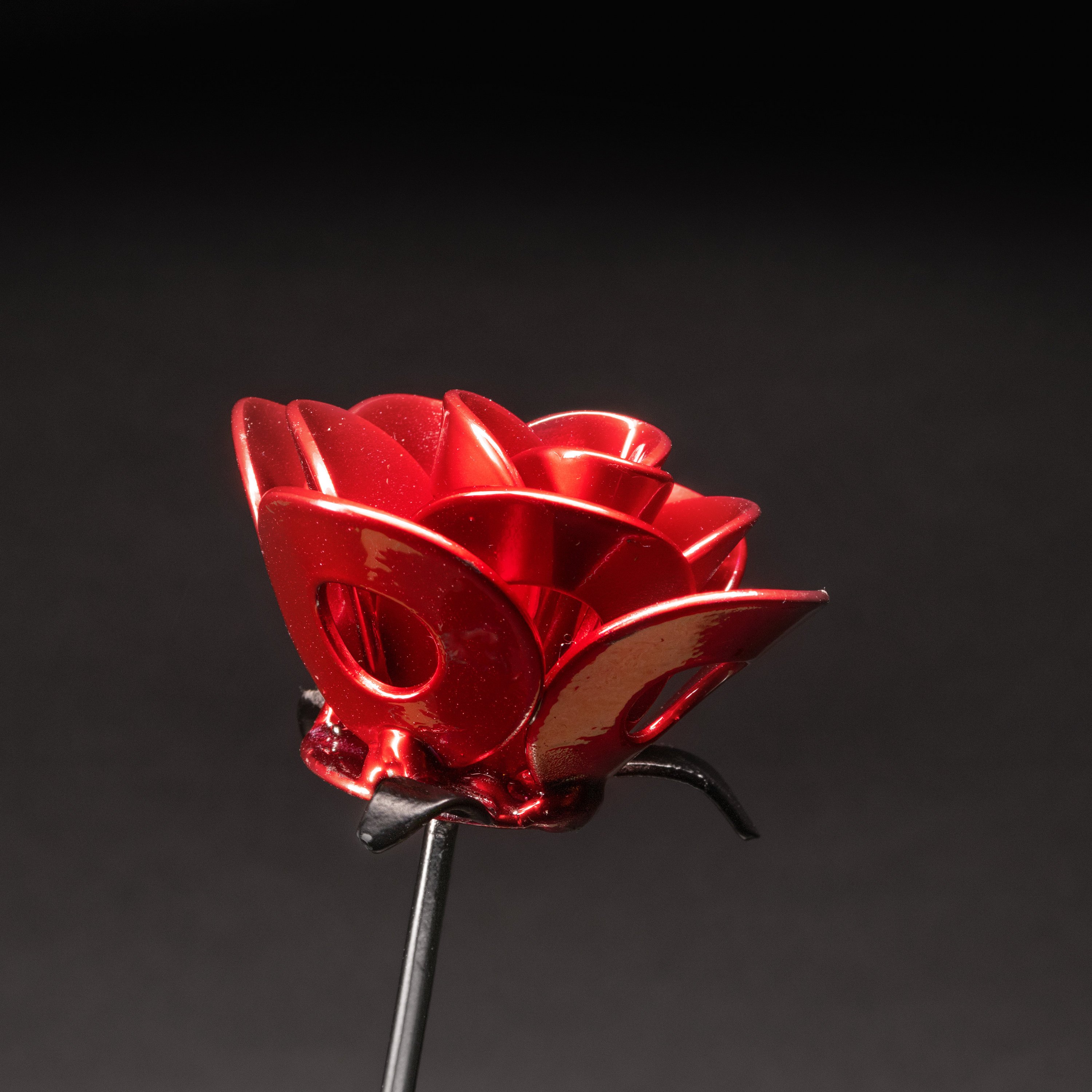 A handcrafted red and black metal rose made from recycled washers and wire, showcasing a lustrous metallic finish and a light green stem, elegantly packaged in a clear gift box.