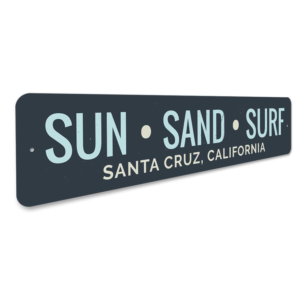 A decorative Sun Sand Surf Sign made of aluminum, featuring beach-themed graphics and customizable text, perfect for coastal decor.