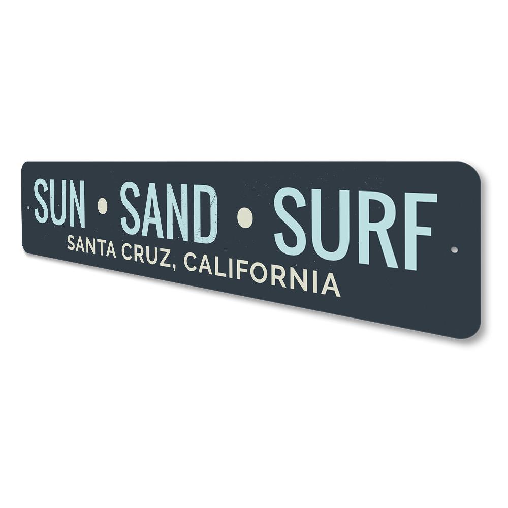 A decorative Sun Sand Surf Sign made of aluminum, featuring beach-themed graphics and customizable text, perfect for coastal decor.