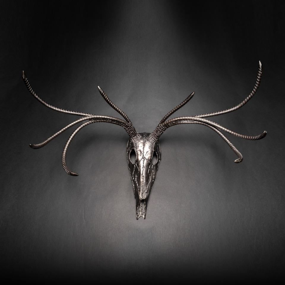 Handcrafted metal sculpture of an eight-point buck skull, showcasing intricate details and a rustic finish.