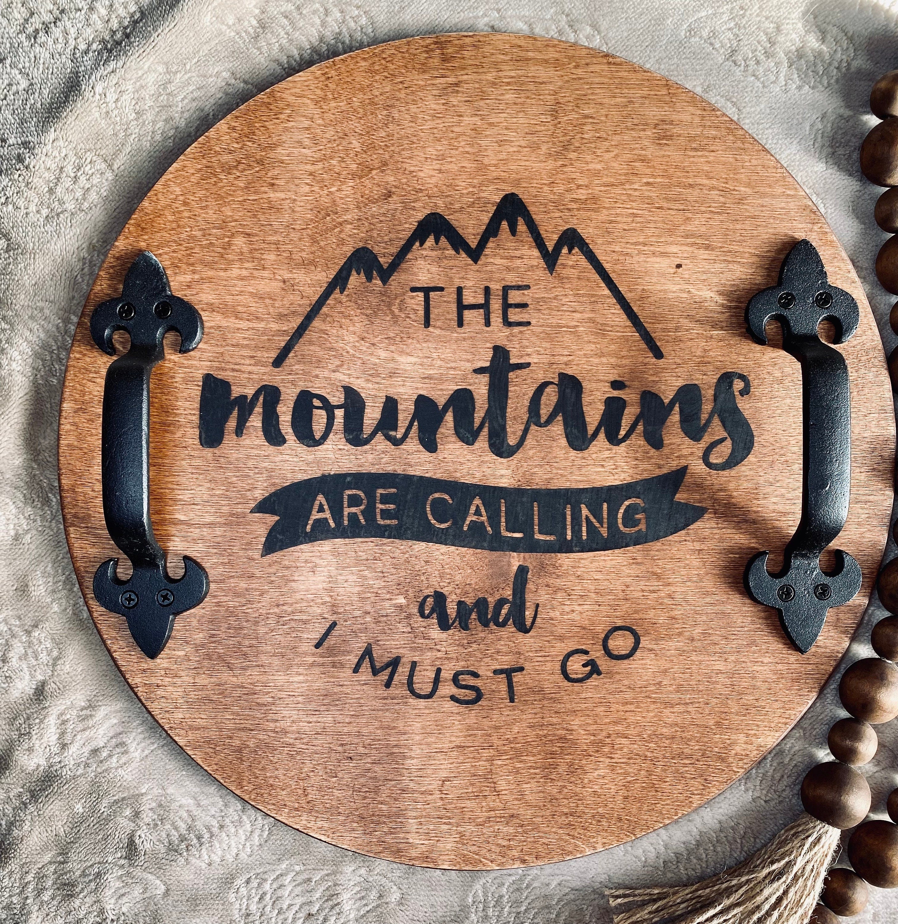 Handmade wooden serving tray with 'The Mountains Are Calling' burned design, featuring black metal handles and customizable stain options.