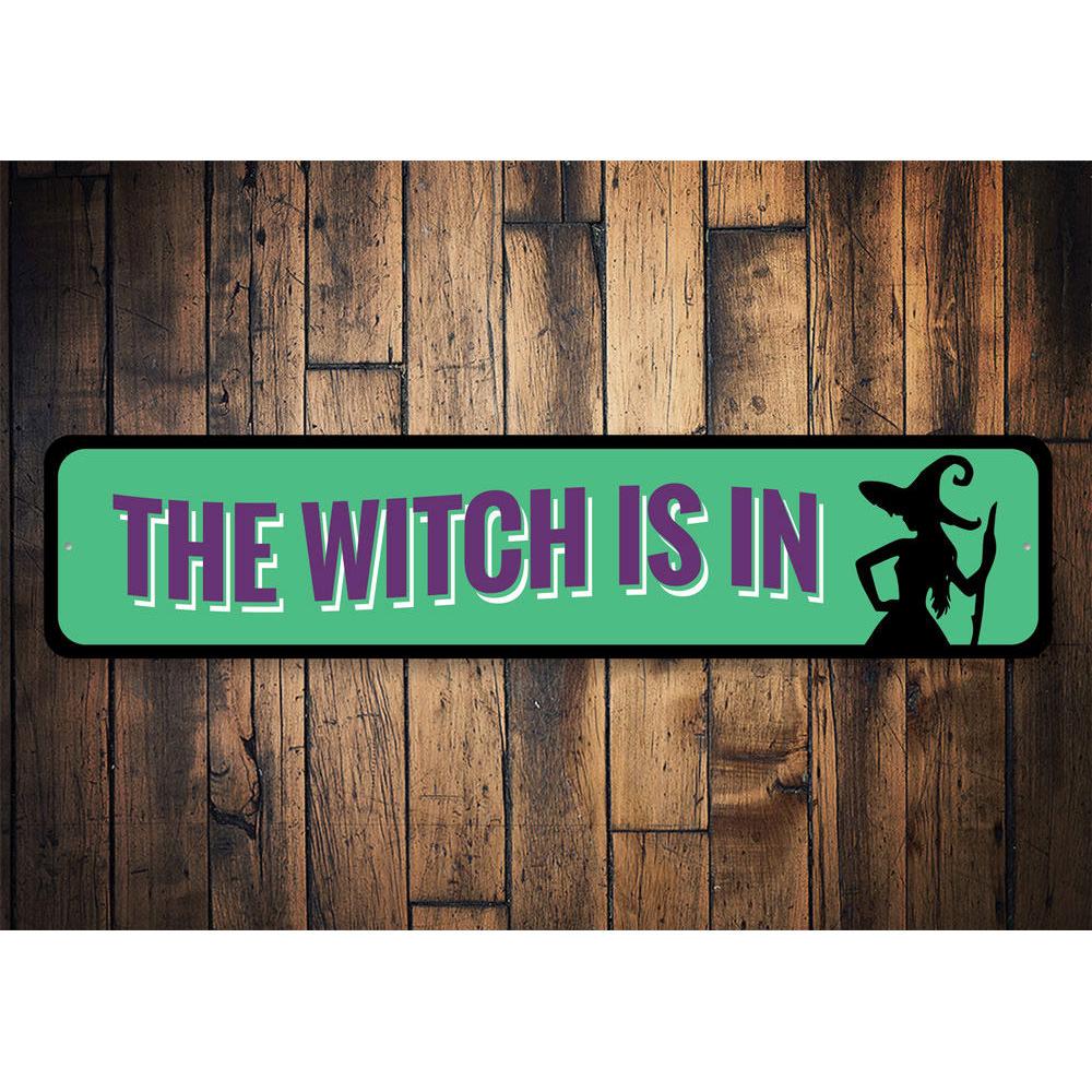 A decorative 'The Witch is IN' sign made of high-quality aluminum, featuring spooky Halloween-themed design, perfect for indoor and outdoor use.