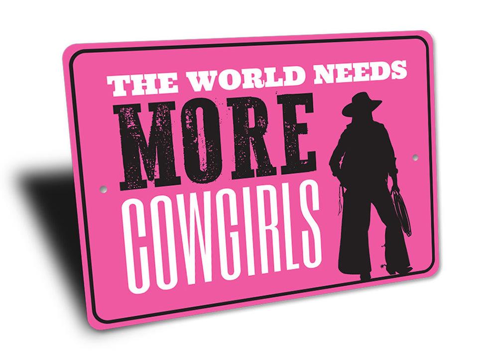 A decorative metal sign reading 'The World Needs More Cowgirls', showcasing a rustic design suitable for barns and kitchens.