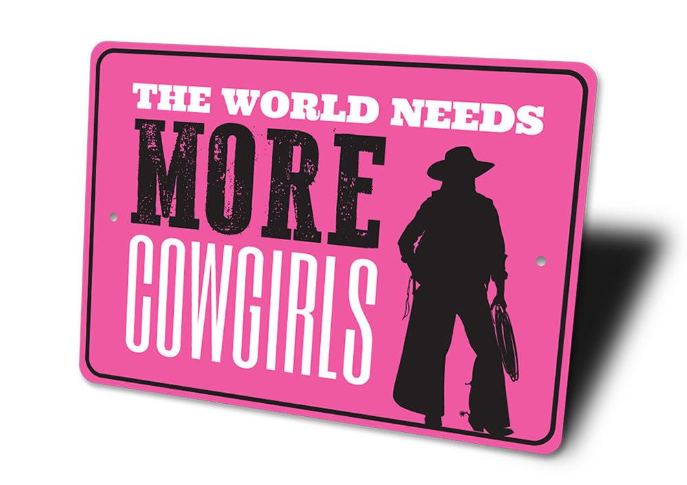 A decorative metal sign reading 'The World Needs More Cowgirls', showcasing a rustic design suitable for barns and kitchens.