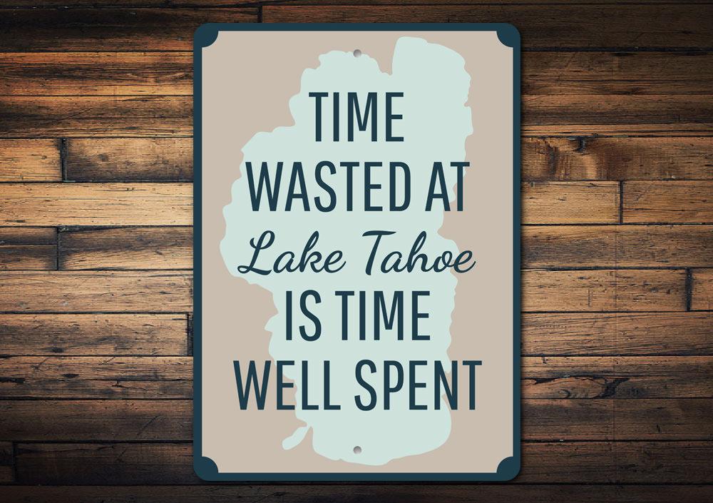 A decorative aluminum sign reading 'Time Wasted at Lake Tahoe', showcasing a beautiful lake scene, perfect for lakehouse decor.