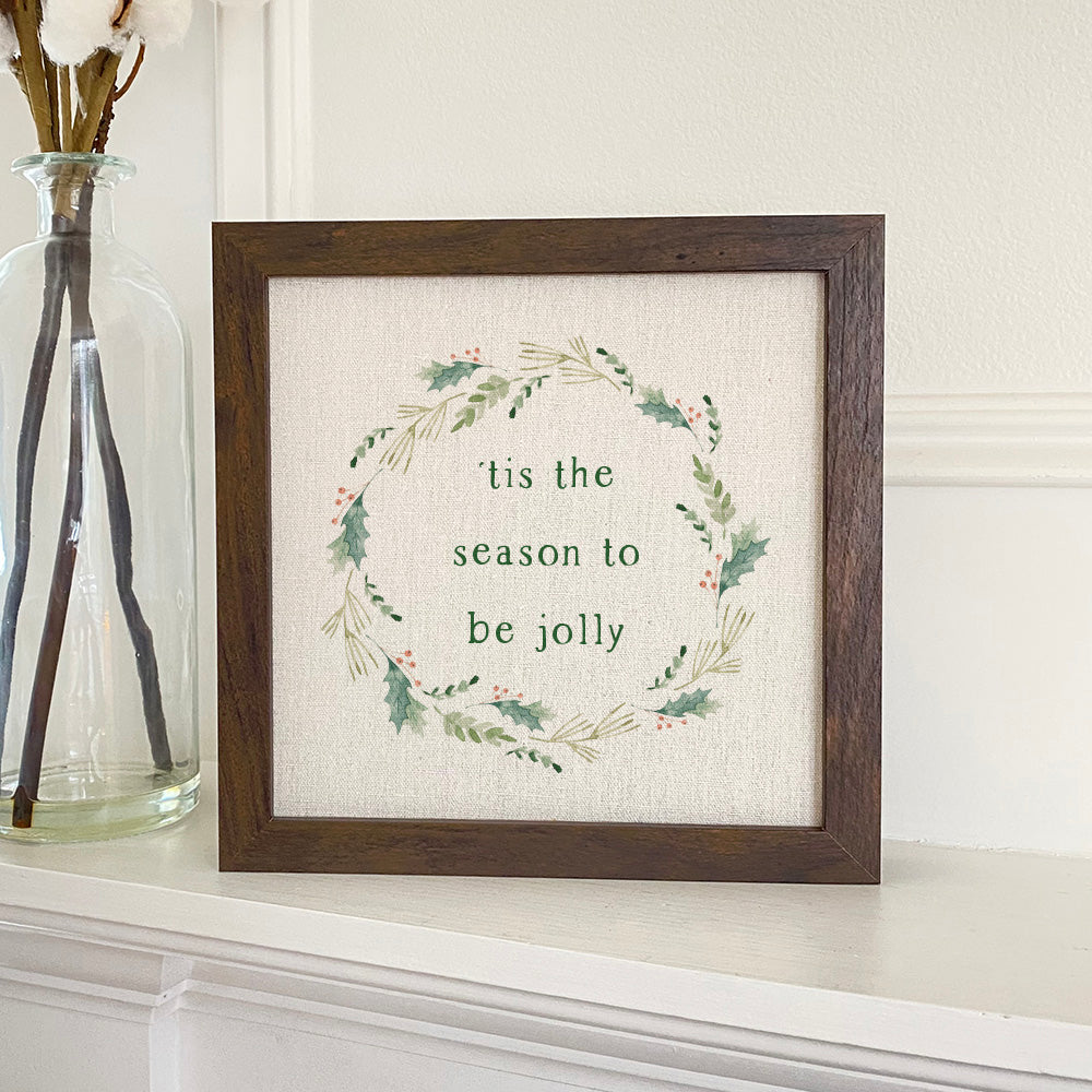 Tis The Season Wreath framed sign with a stylized wood frame, eco-friendly ink printing, and a linen-look neutral background.
