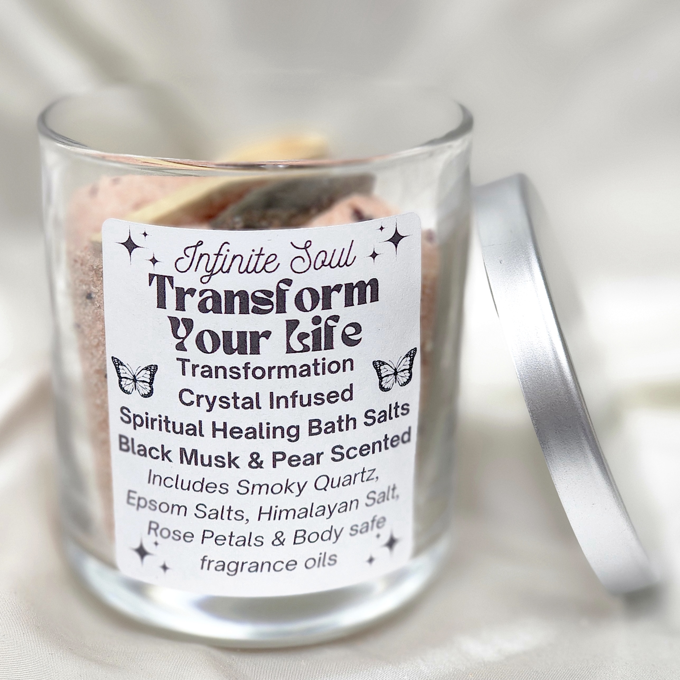 A jar of Transformation Crystal Infused Bath Salt in Black, featuring Malachite crystals and rose petals, with a wooden spoon beside it.