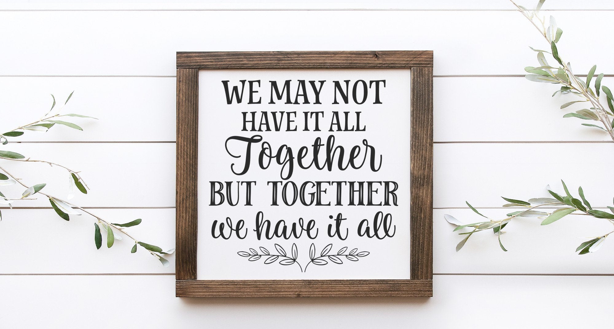 A handmade wooden sign with a white background and black lettering that reads 'We May Not Have It All Together But Together We Have It All'.