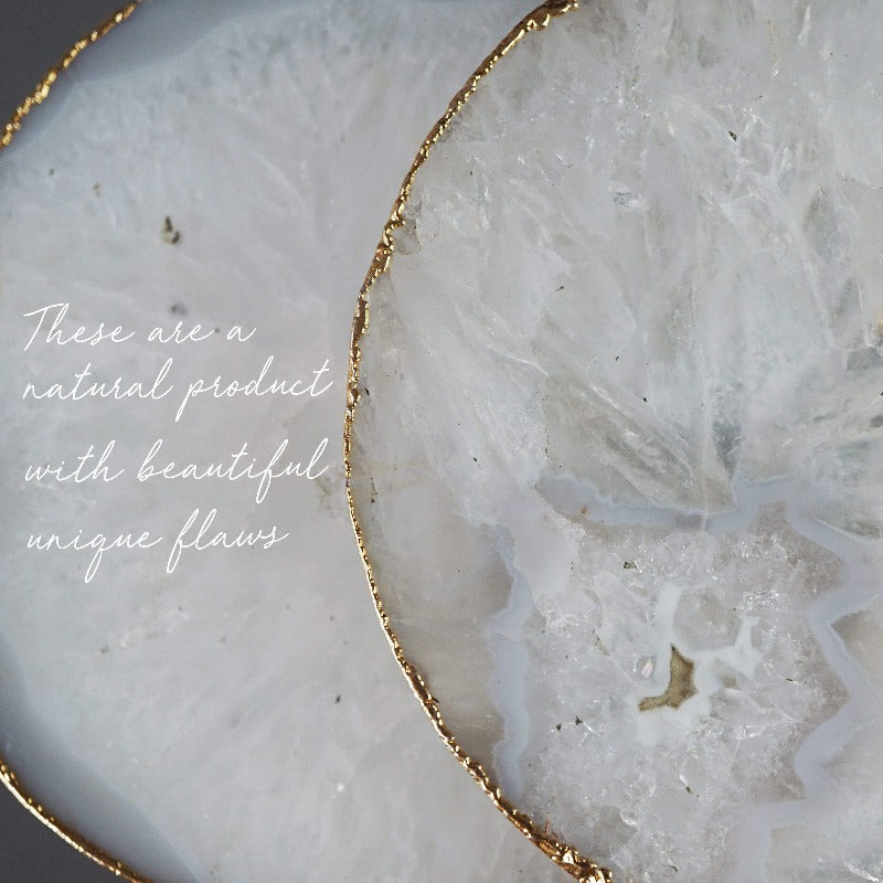 A set of two white crystal agate coasters with gilded edges in gold, rose gold, and silver, showcasing unique natural patterns.