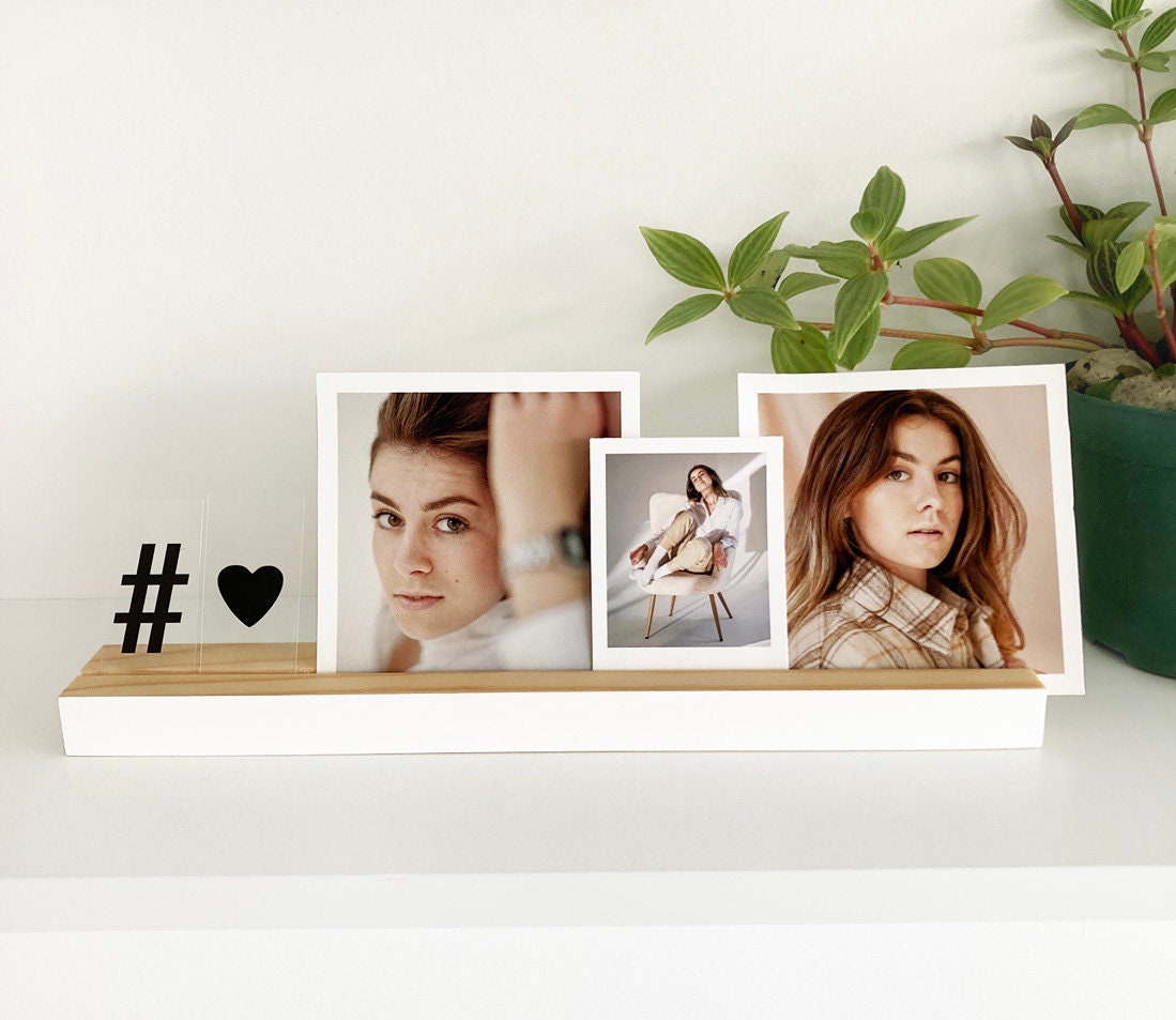 A stylish white wood photo ledge displaying various photos and art prints, showcasing its versatility and elegant design.
