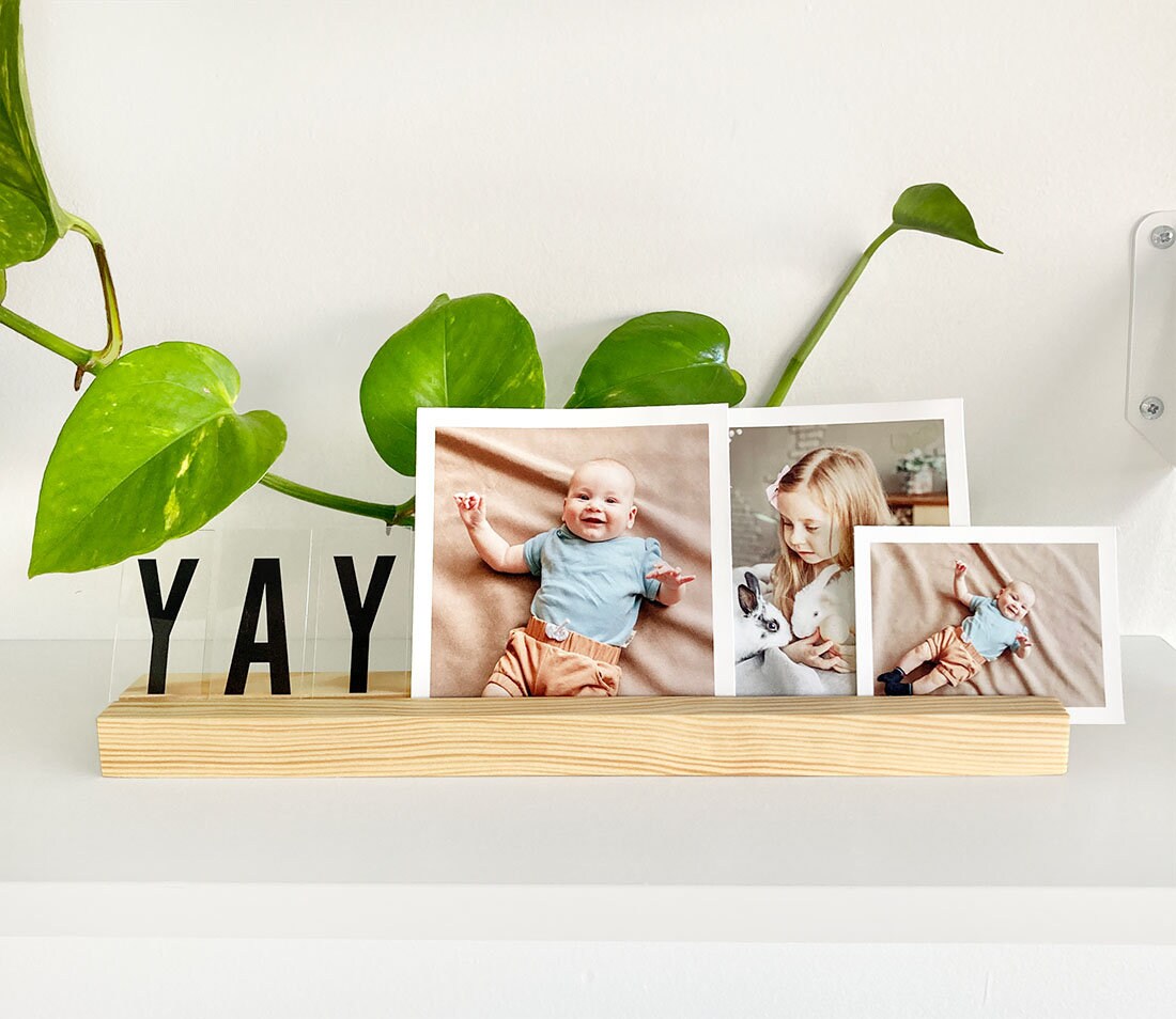 A stylish white wood photo ledge displaying various photos and art prints, showcasing its versatility and elegant design.