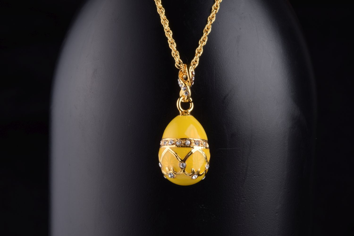 A beautiful yellow egg pendant necklace adorned with Austrian crystals and plated with 24K gold, elegantly displayed on a black background.