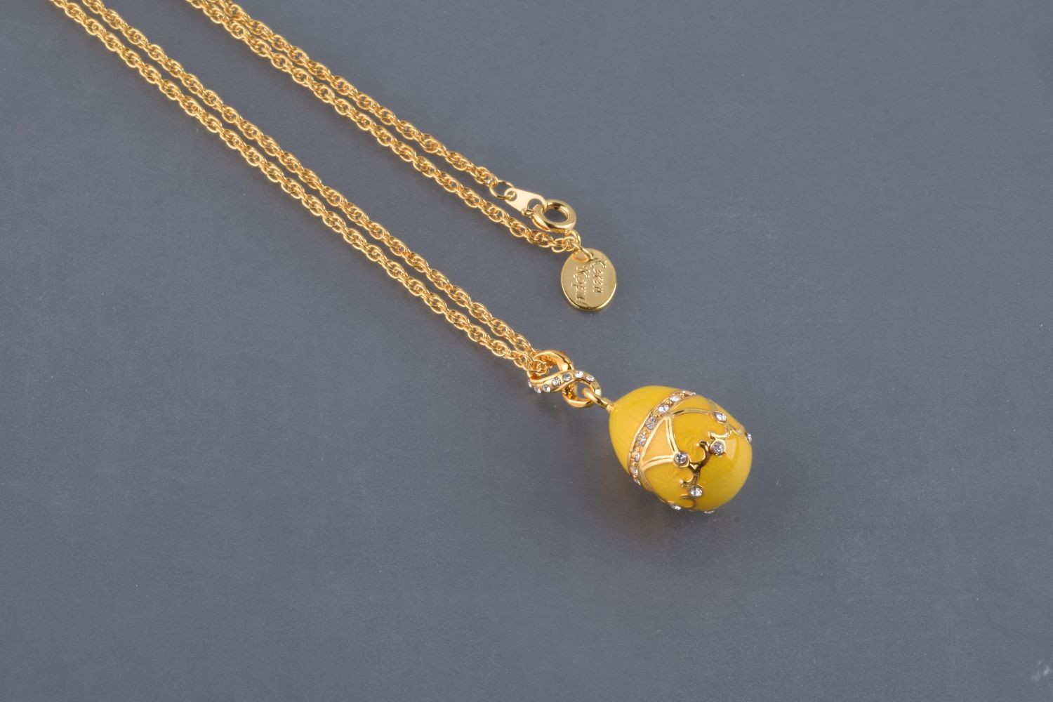 A beautiful yellow egg pendant necklace adorned with Austrian crystals and plated with 24K gold, elegantly displayed on a black background.