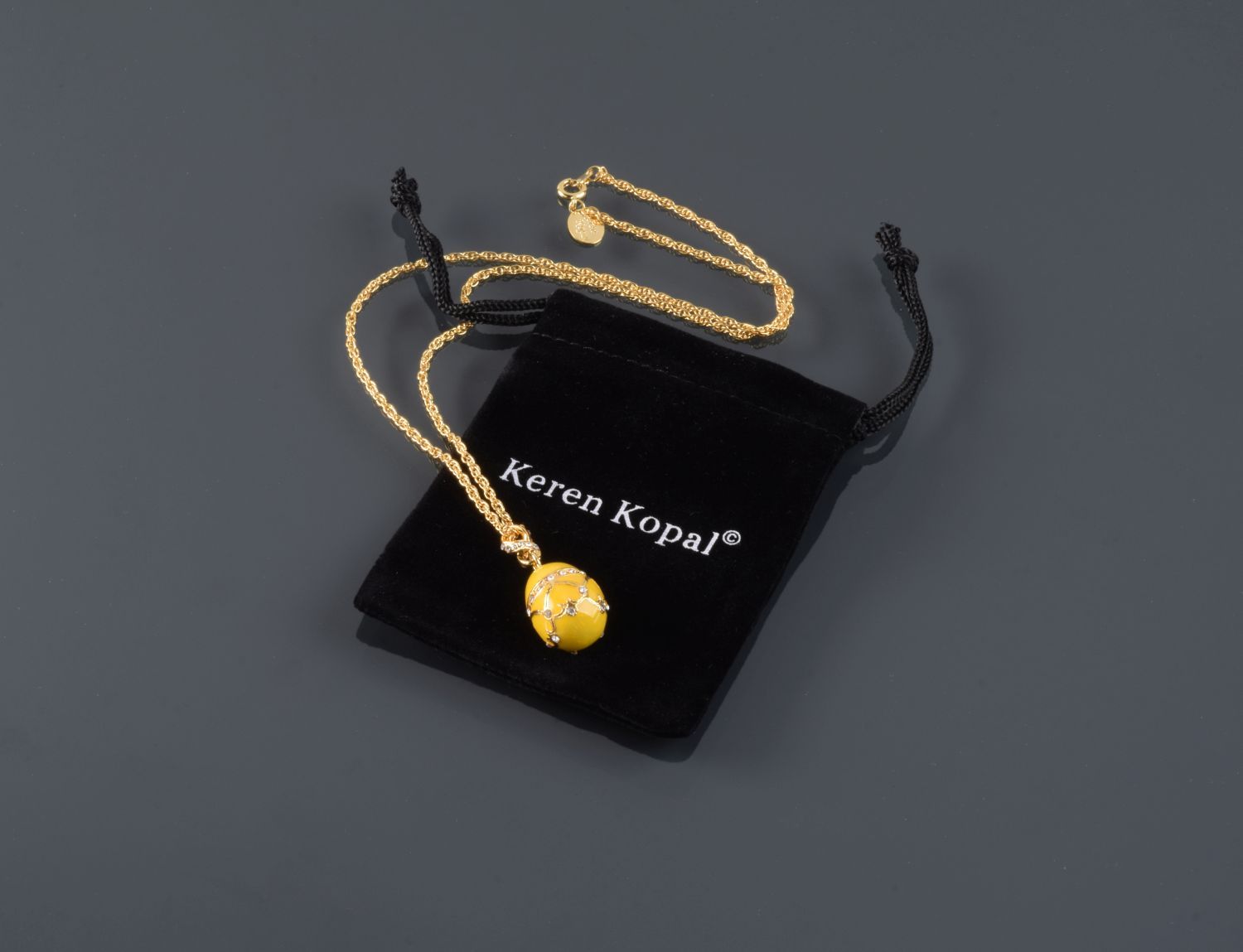 A beautiful yellow egg pendant necklace adorned with Austrian crystals and plated with 24K gold, elegantly displayed on a black background.