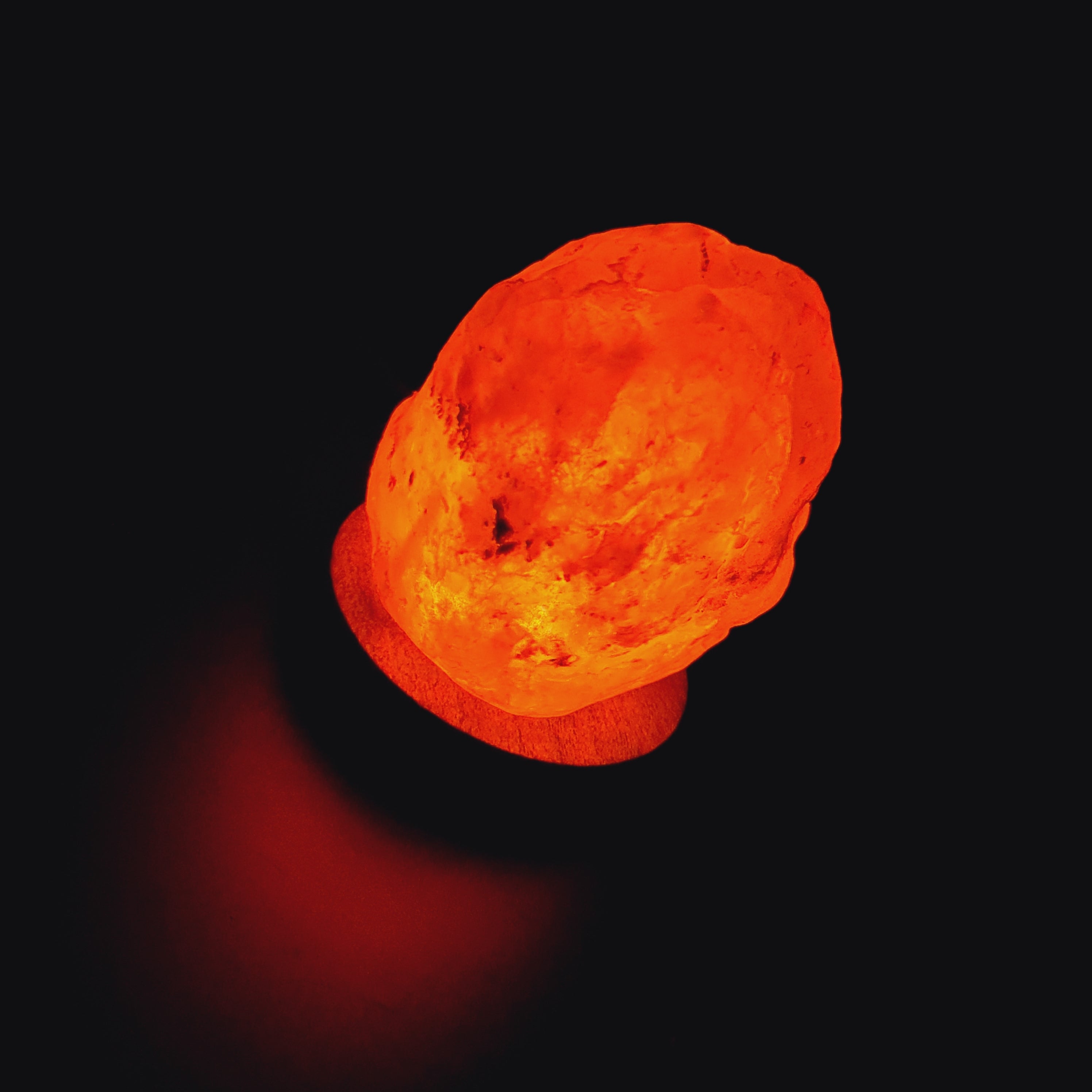 Himalaya Salzlampe aus rosa Salz mit wechselnden Farben auf Holzsockel, strahlt warmes Bernsteinlicht aus.