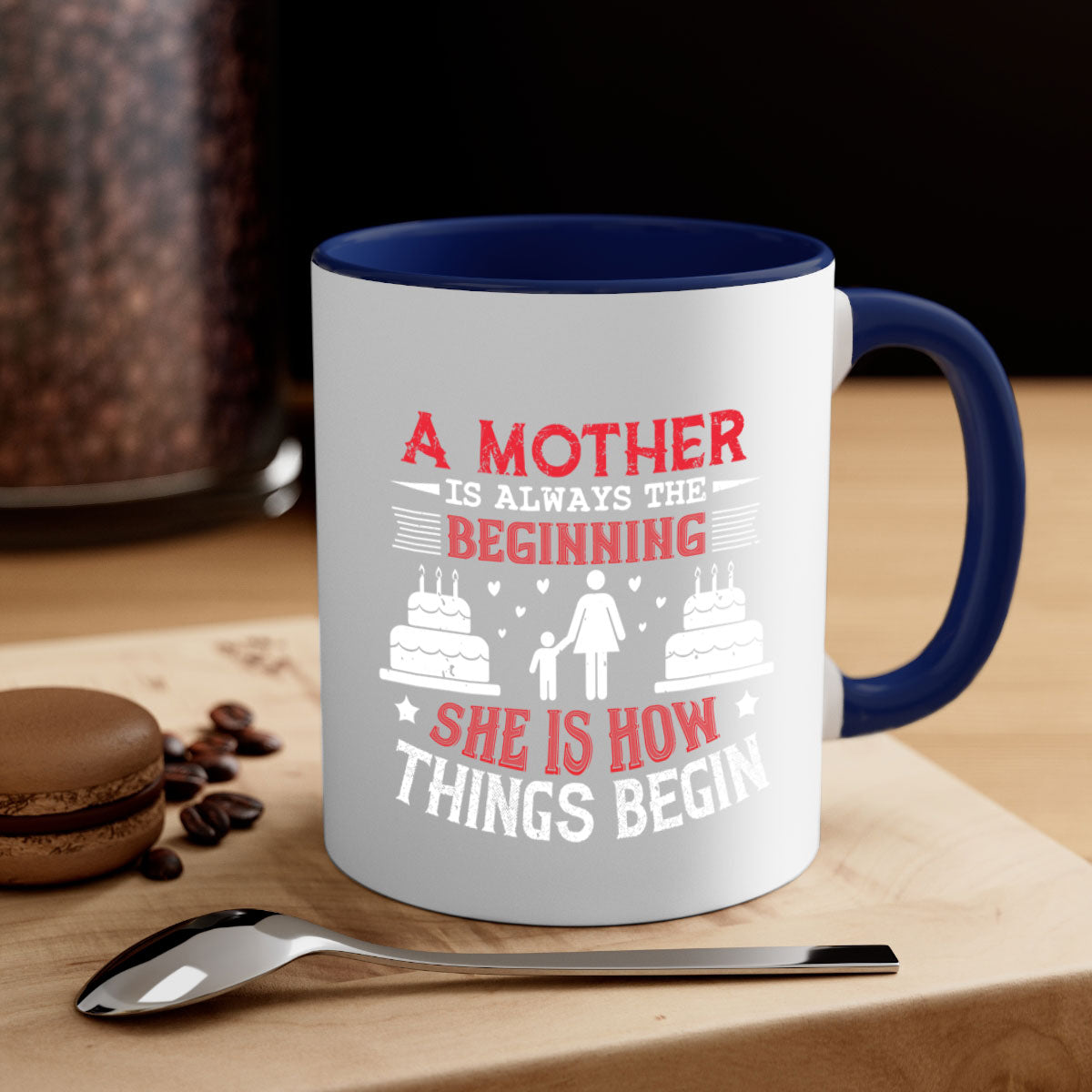A two-tone ceramic coffee mug with a colored handle and glossy finish, featuring the text 'A Mother is Always the Beginning' for Mother's Day.