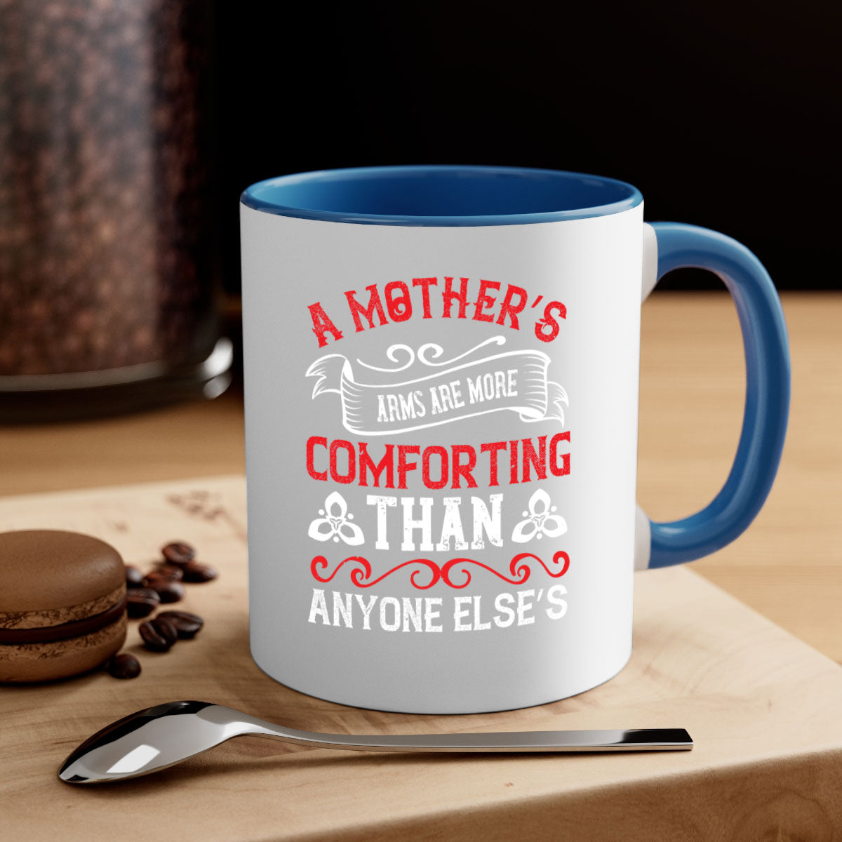A two-tone ceramic mug with a colored handle and interior, featuring the phrase 'A Mother’s Arms Are More Comforting Than Anyone Else’s'.