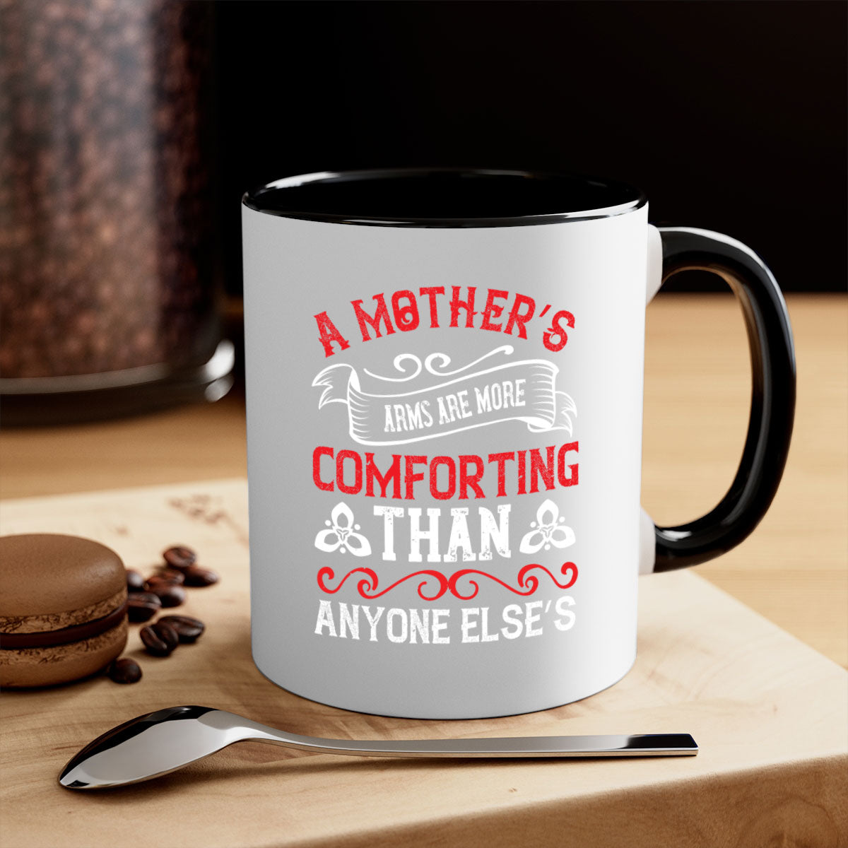 A two-tone ceramic mug with a colored handle and interior, featuring the phrase 'A Mother’s Arms Are More Comforting Than Anyone Else’s'.