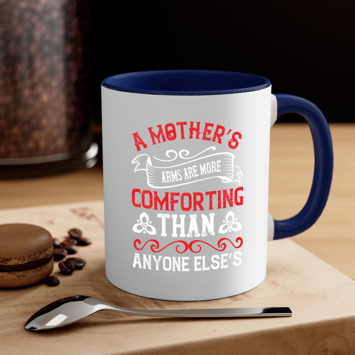 A two-tone ceramic mug with a colored handle and interior, featuring the phrase 'A Mother’s Arms Are More Comforting Than Anyone Else’s'.