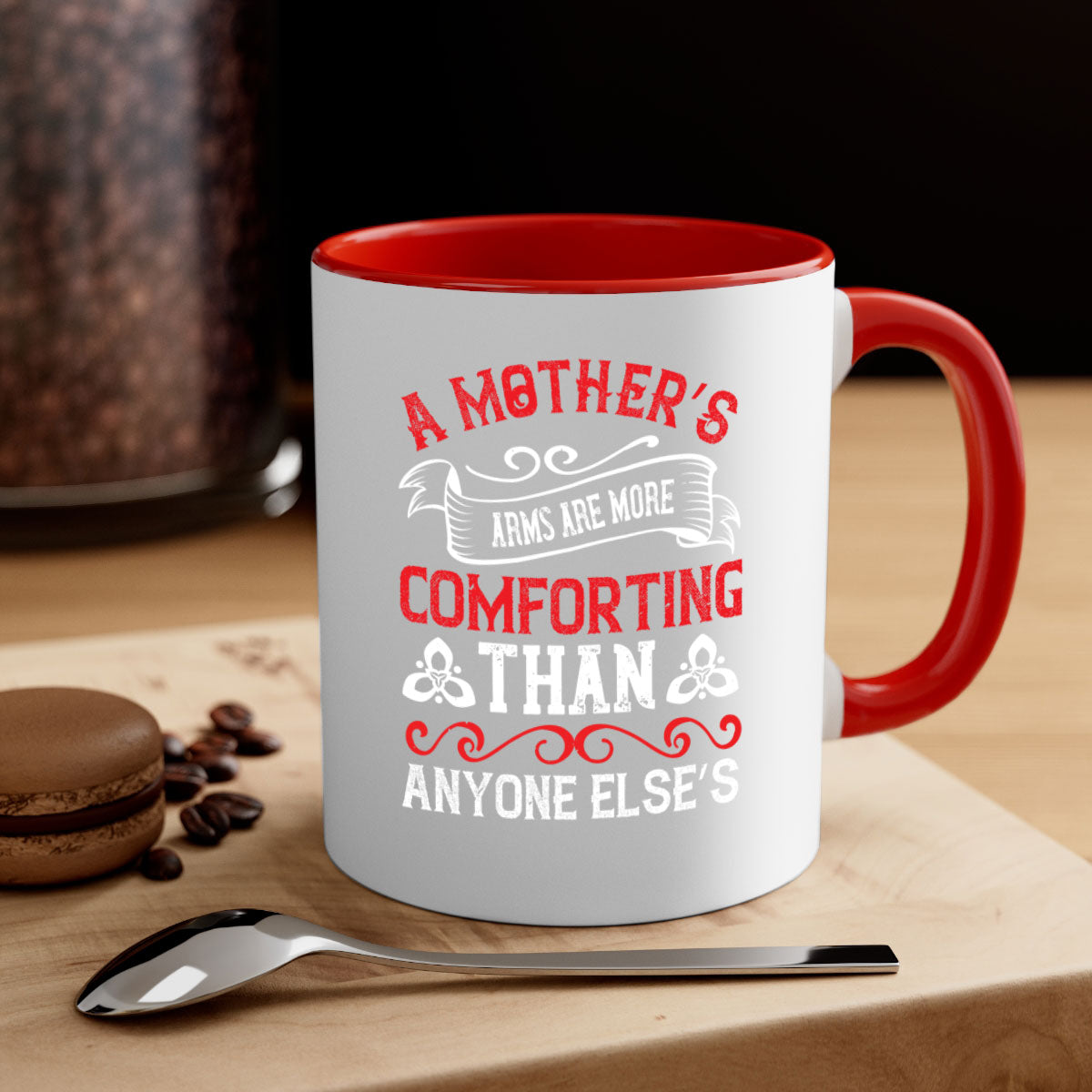 A two-tone ceramic mug with a colored handle and interior, featuring the phrase 'A Mother’s Arms Are More Comforting Than Anyone Else’s'.