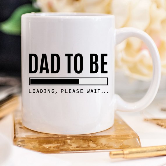 A humorous Baby Announcement Mug featuring 'Dad To Be. Loading, Please W' design, perfect for future dads.