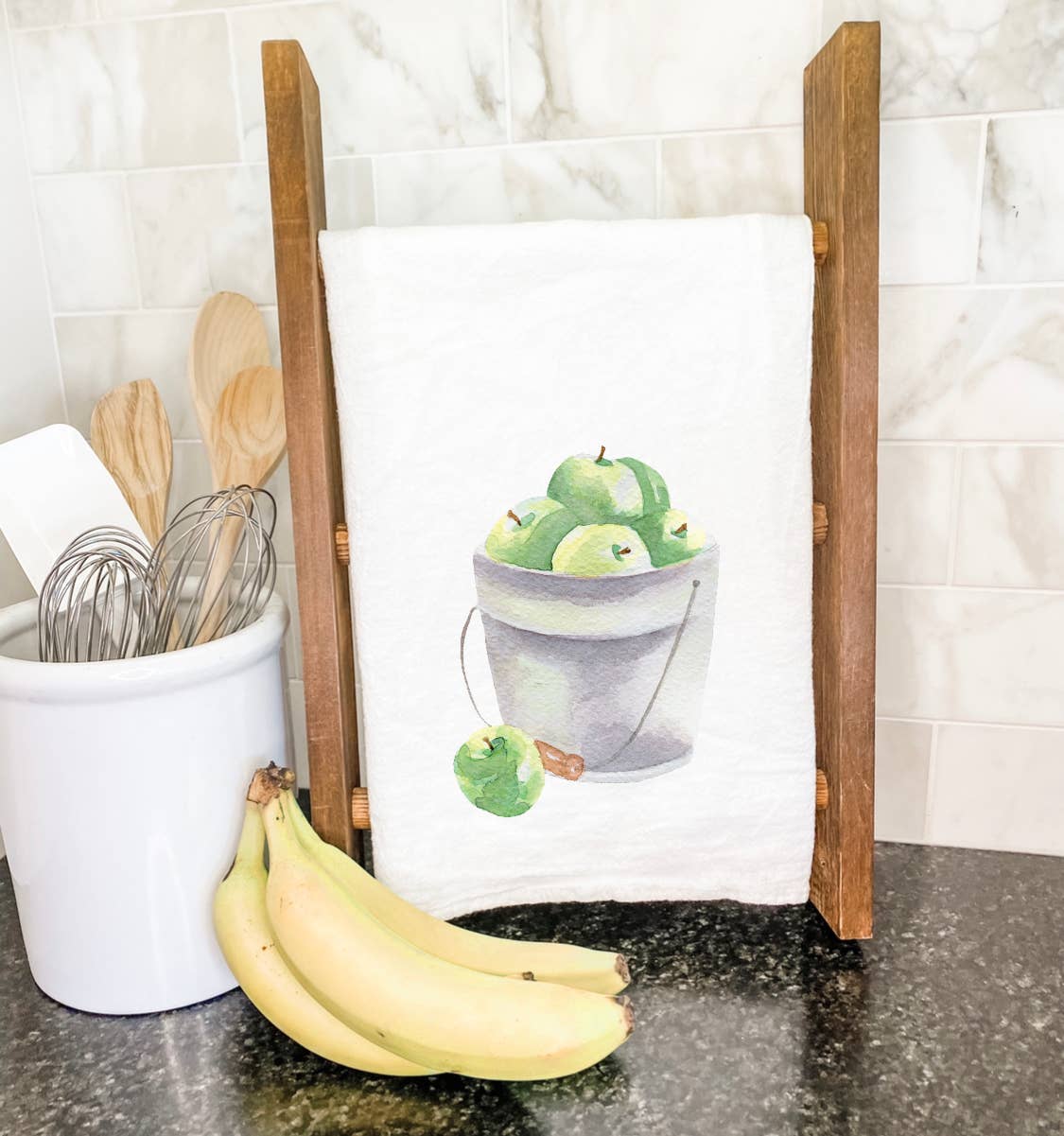 A vibrant cotton tea towel featuring a bucket of green apples design, perfect for kitchen use.