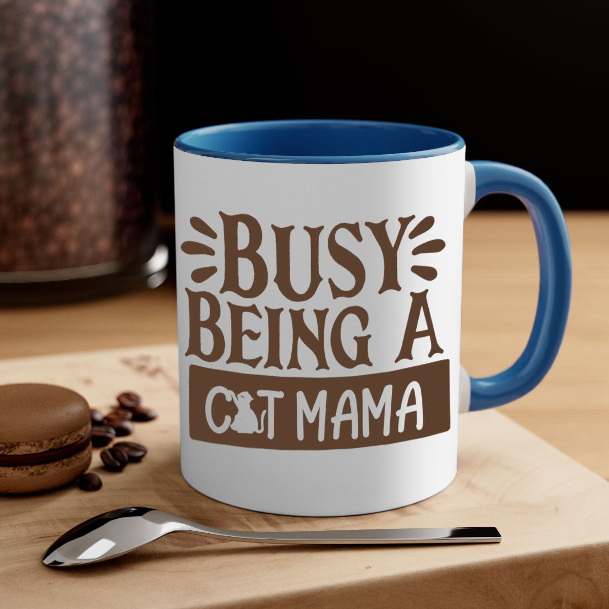 A two-tone ceramic mug with a colored handle and interior, featuring the phrase 'Busy Being A Cat Mama' in a stylish font.