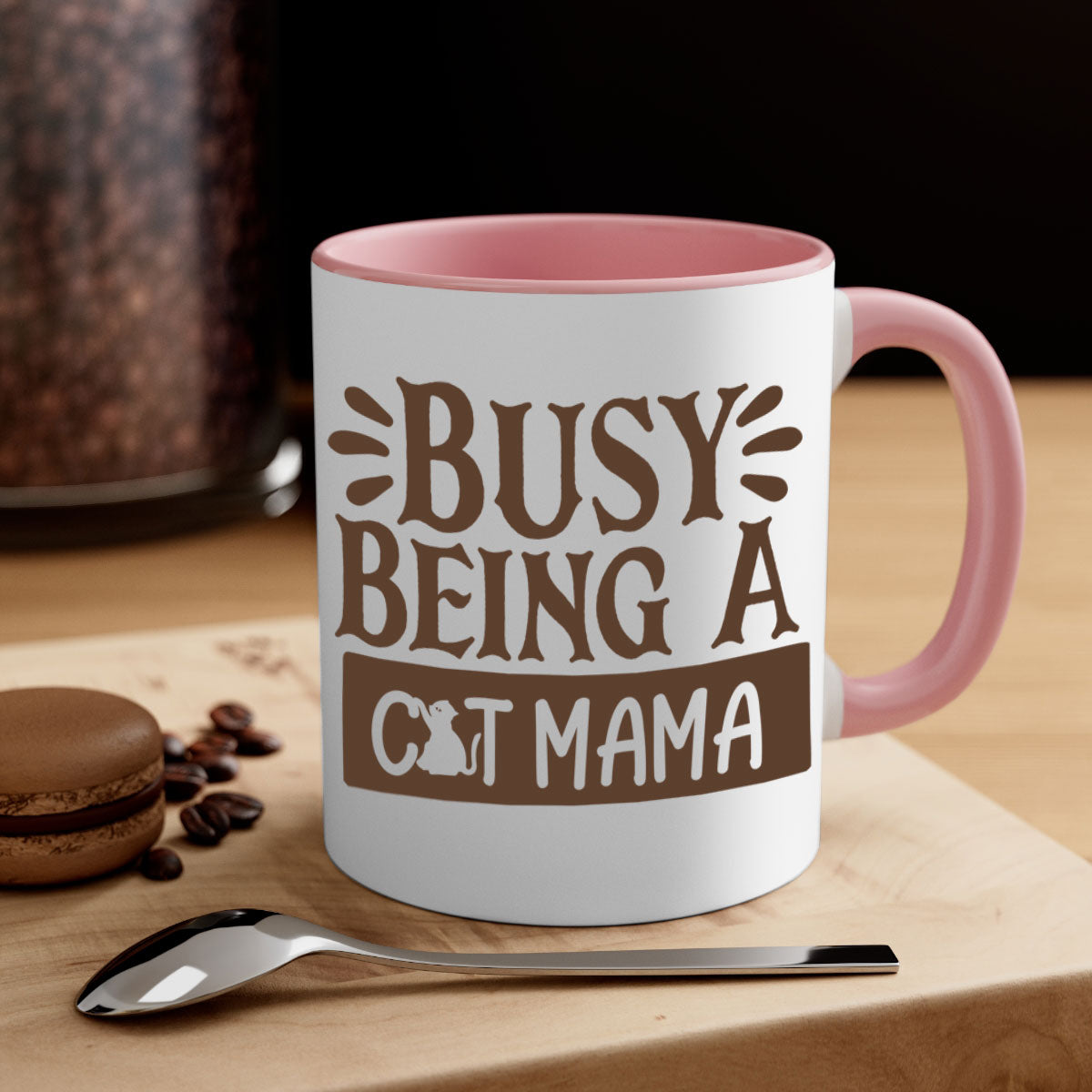 A two-tone ceramic mug with a colored handle and interior, featuring the phrase 'Busy Being A Cat Mama' in a stylish font.