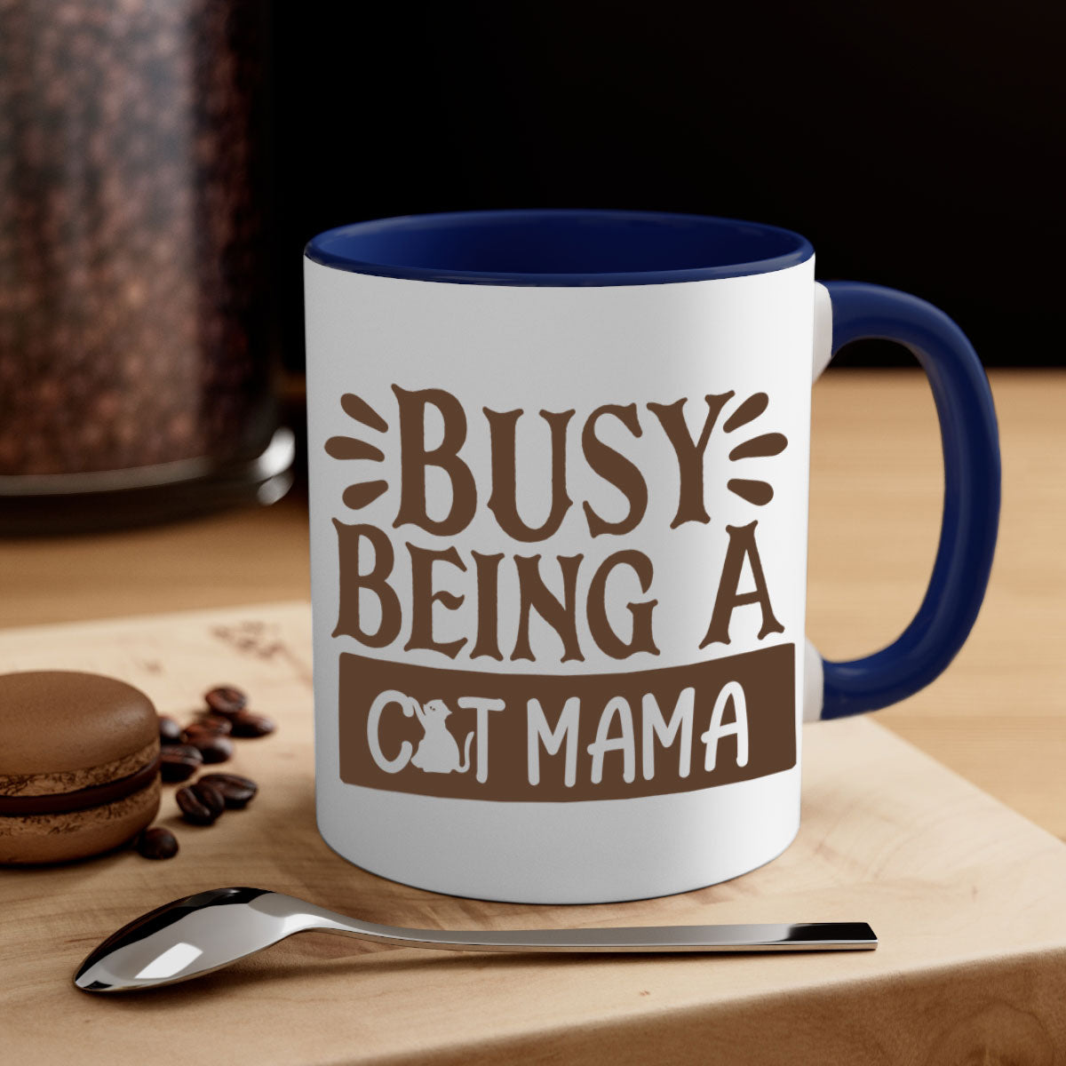 A two-tone ceramic mug with a colored handle and interior, featuring the phrase 'Busy Being A Cat Mama' in a stylish font.
